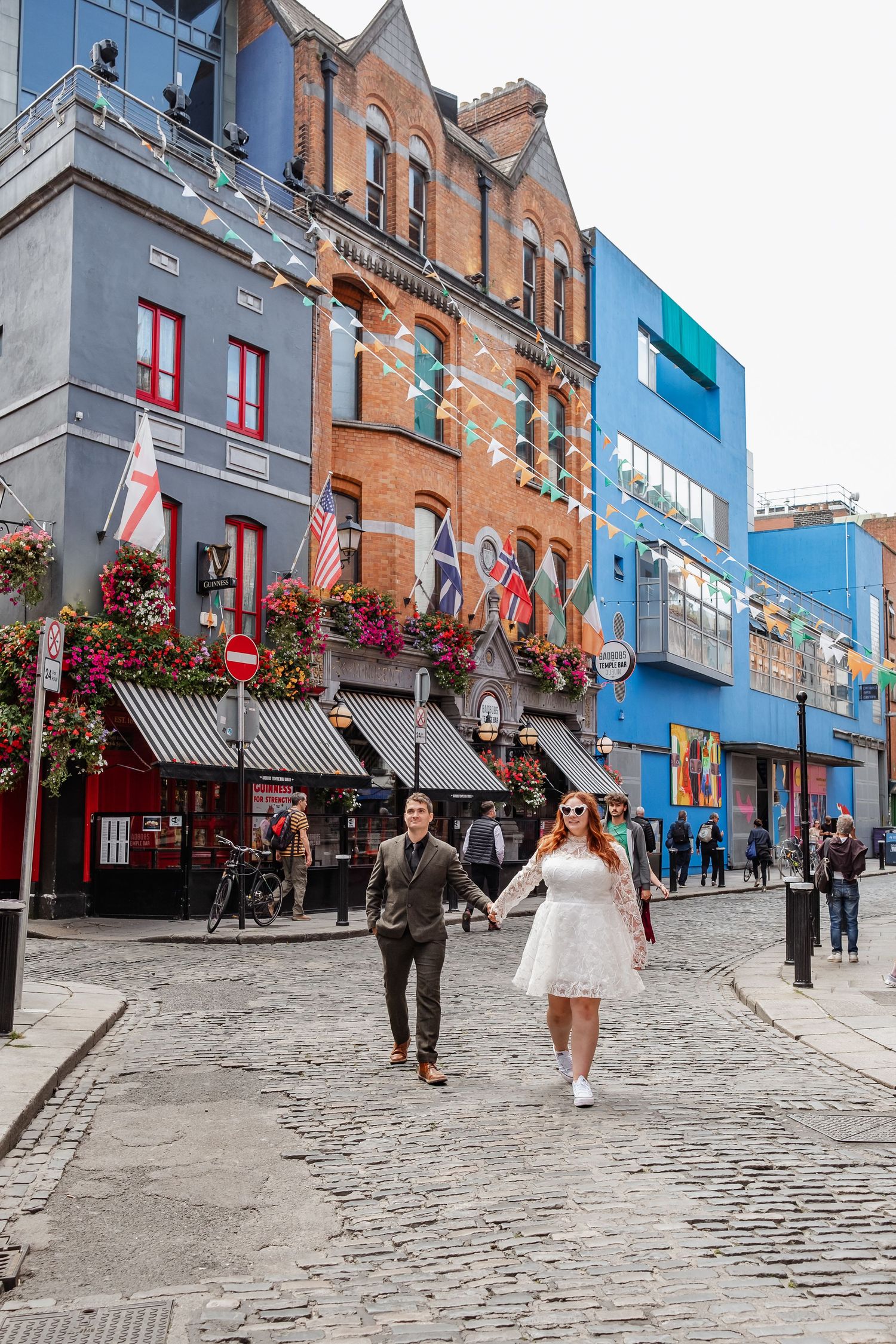 A couple walking on cobblestone street past colorful buildings with flower boxes in Dublin.