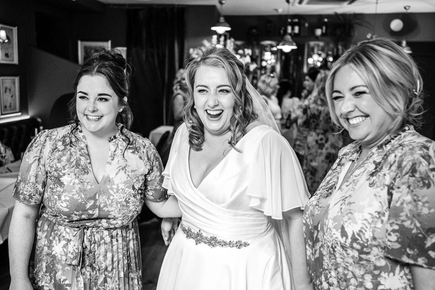 Black and white photo of wedding celebration with guests in floral dresses.