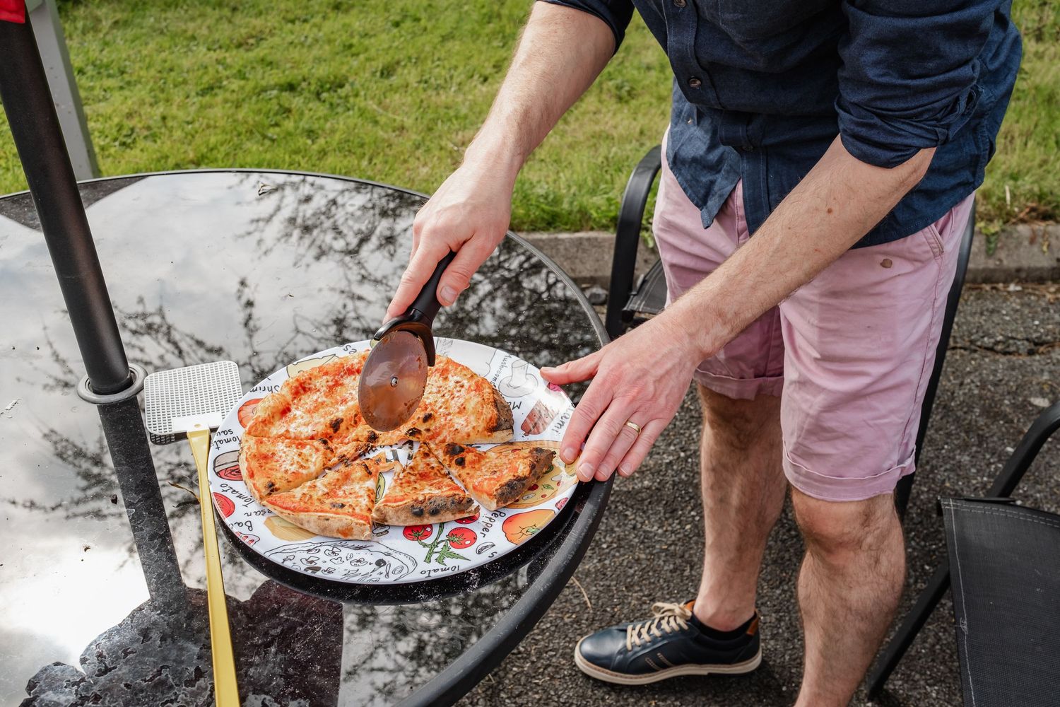 Person serving fresh pizza outdoors on a white plate.