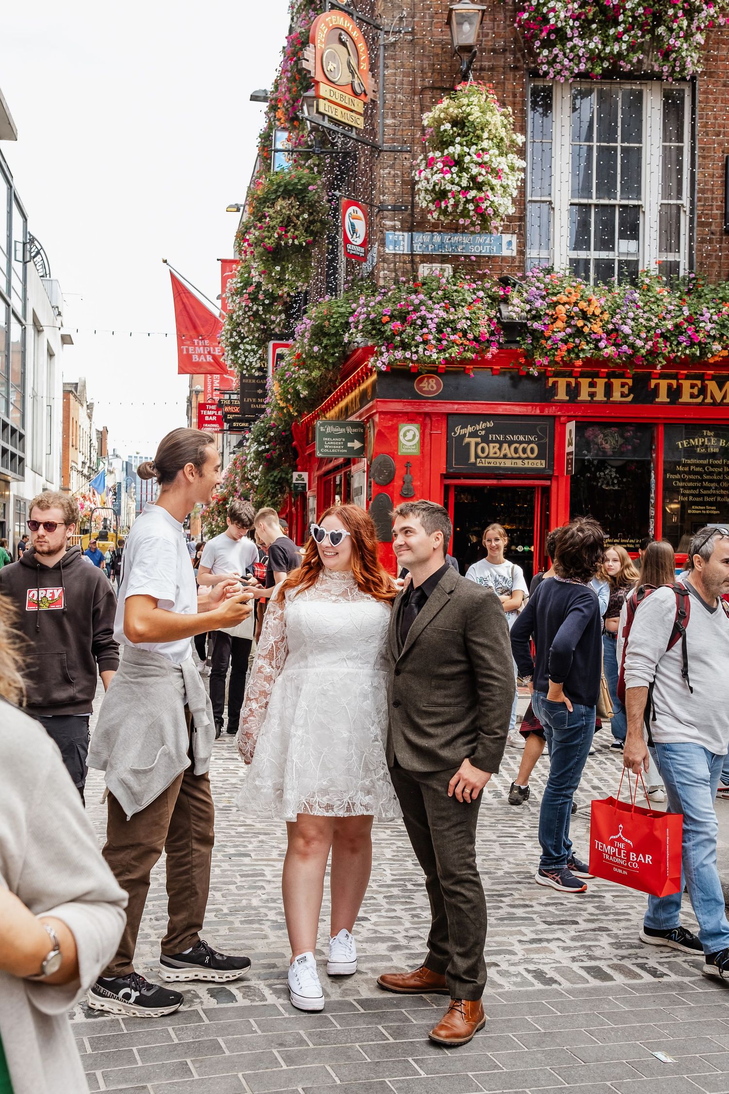 People gathered outside The Temple Bar pub with its distinctive red facade and hanging flowers.