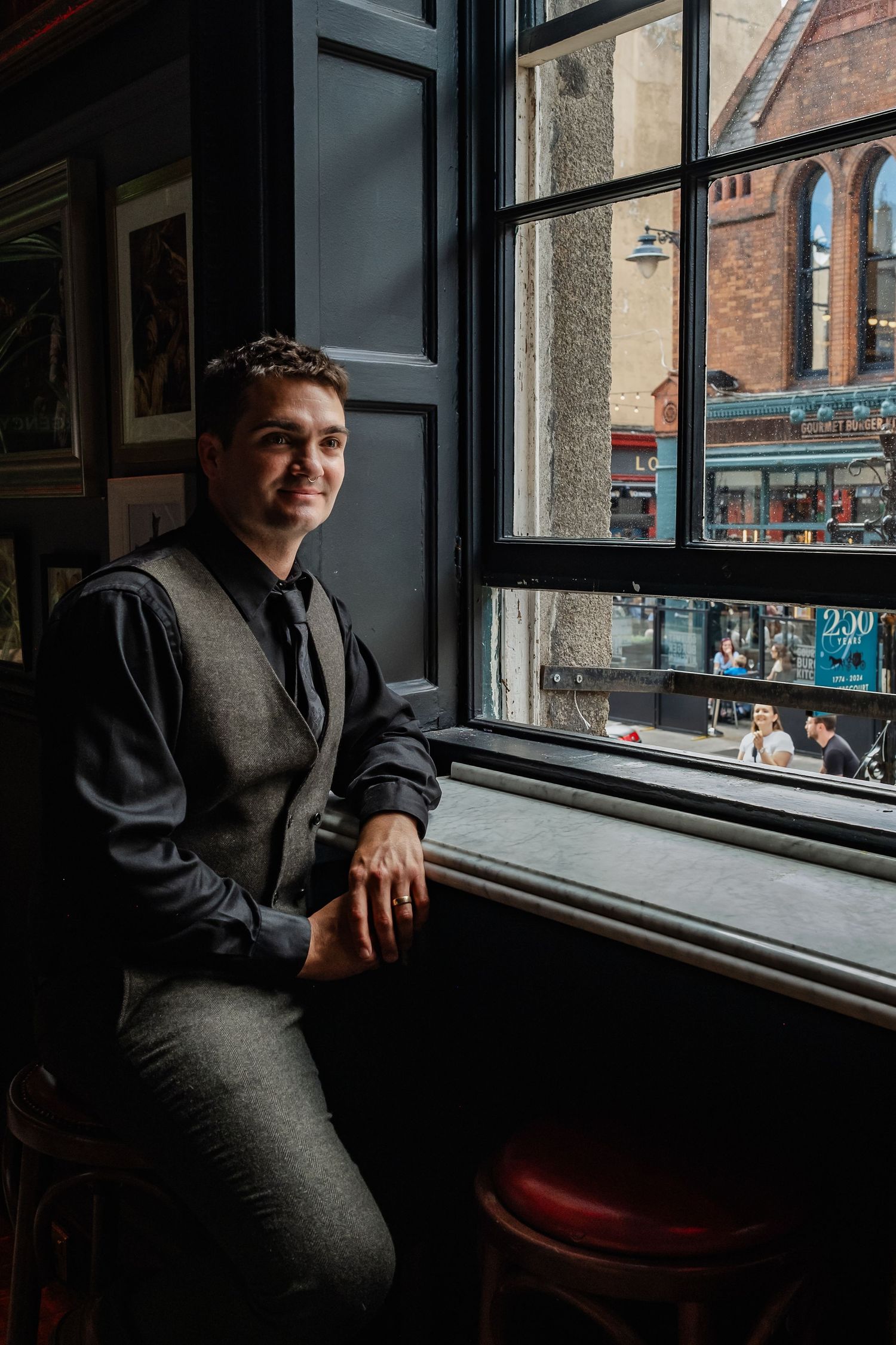 Person in grey suit sitting by window in traditional pub with framed artwork.