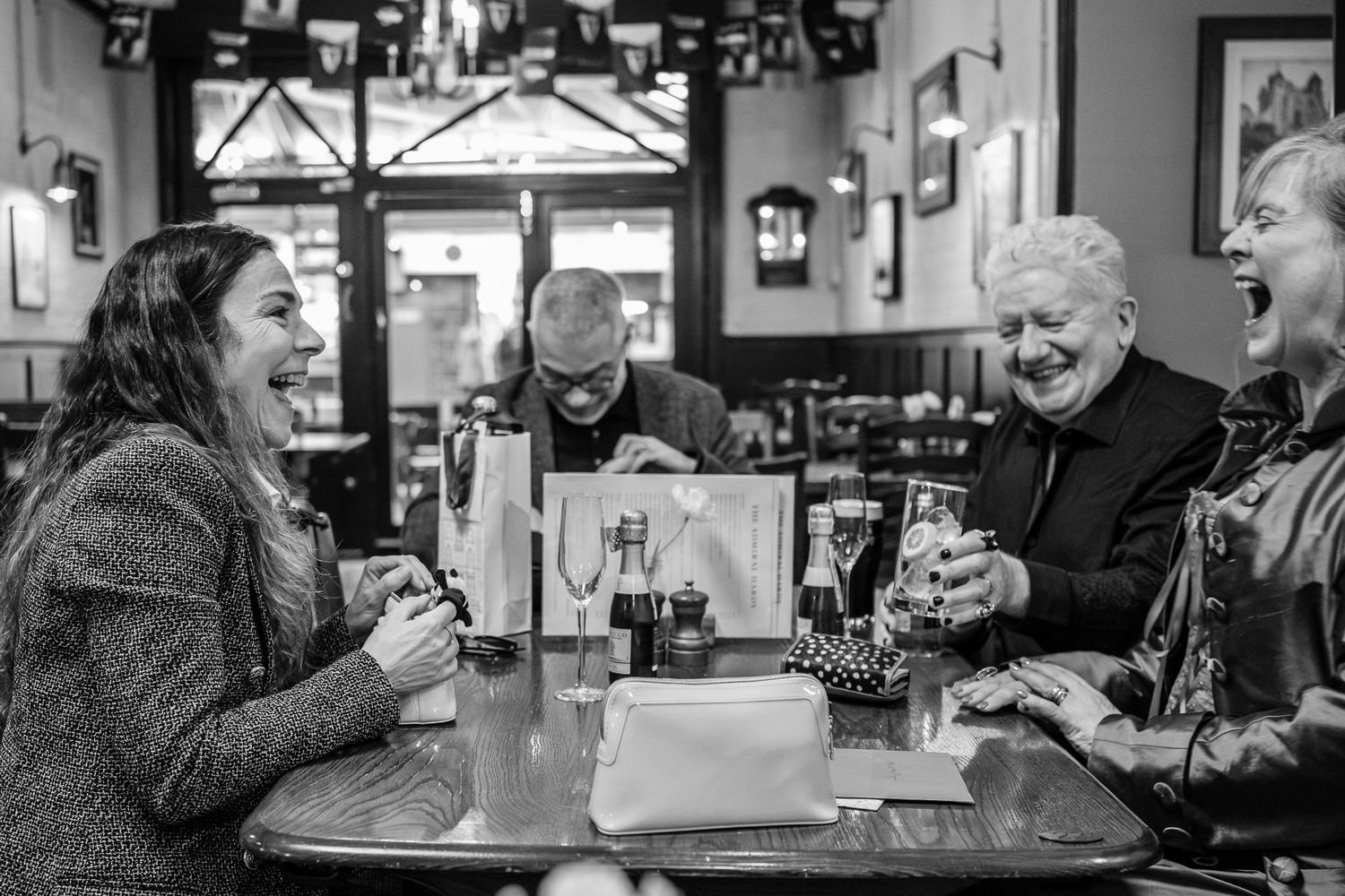 A group enjoying hearty laughter while sitting at a pub table in black and white.