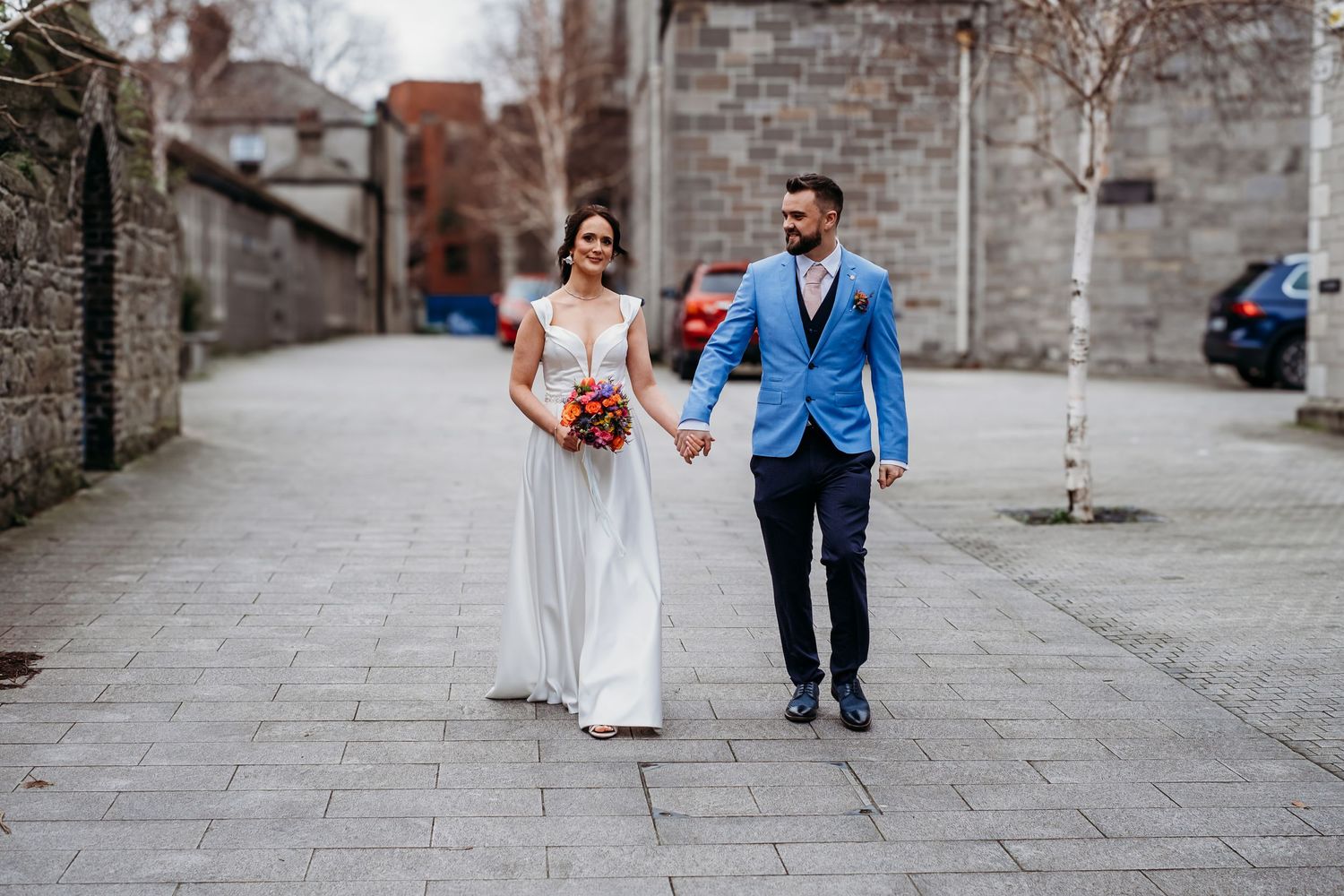 Three people in formal attire stand together outside a brick building.
