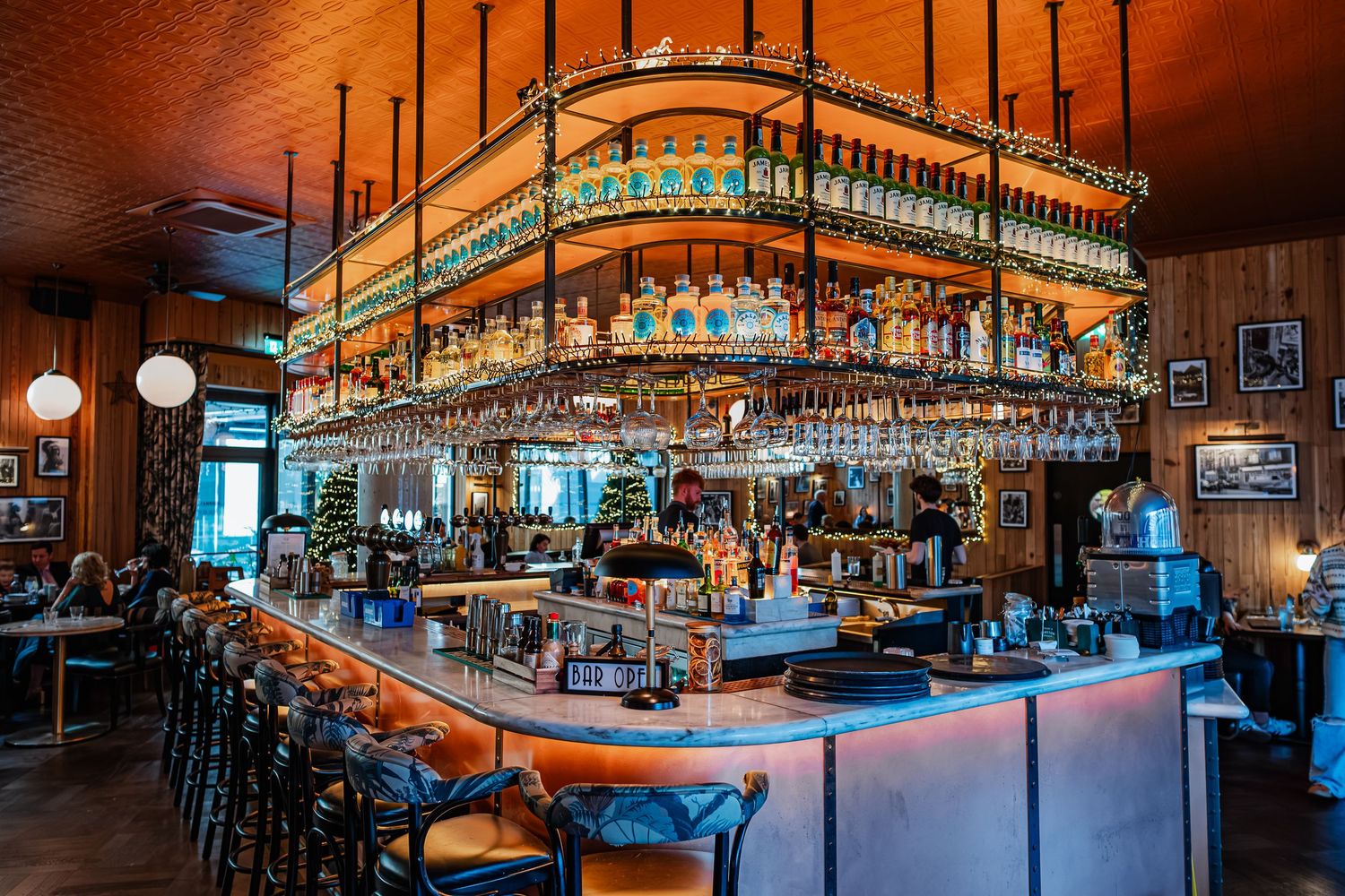 Elegant bar interior with hanging wine glasses, backlit shelves of spirits, and warm wood paneling at a upscale restaurant.