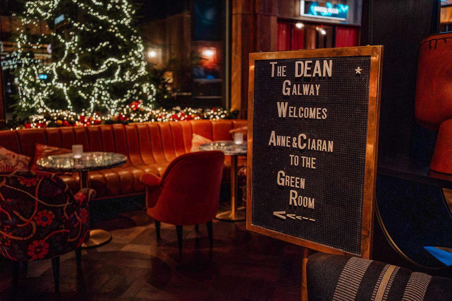 The Dean Galway hotel welcomes guests Anne and Ciaran to the Green Room with festive Christmas decor and cozy red seating.