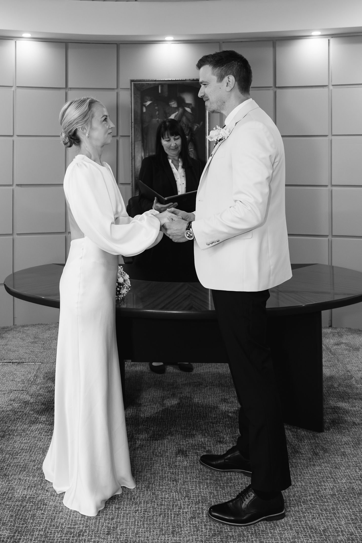 Black and white photo of a bride and groom exchanging vows at a civil wedding ceremony with an officiant.