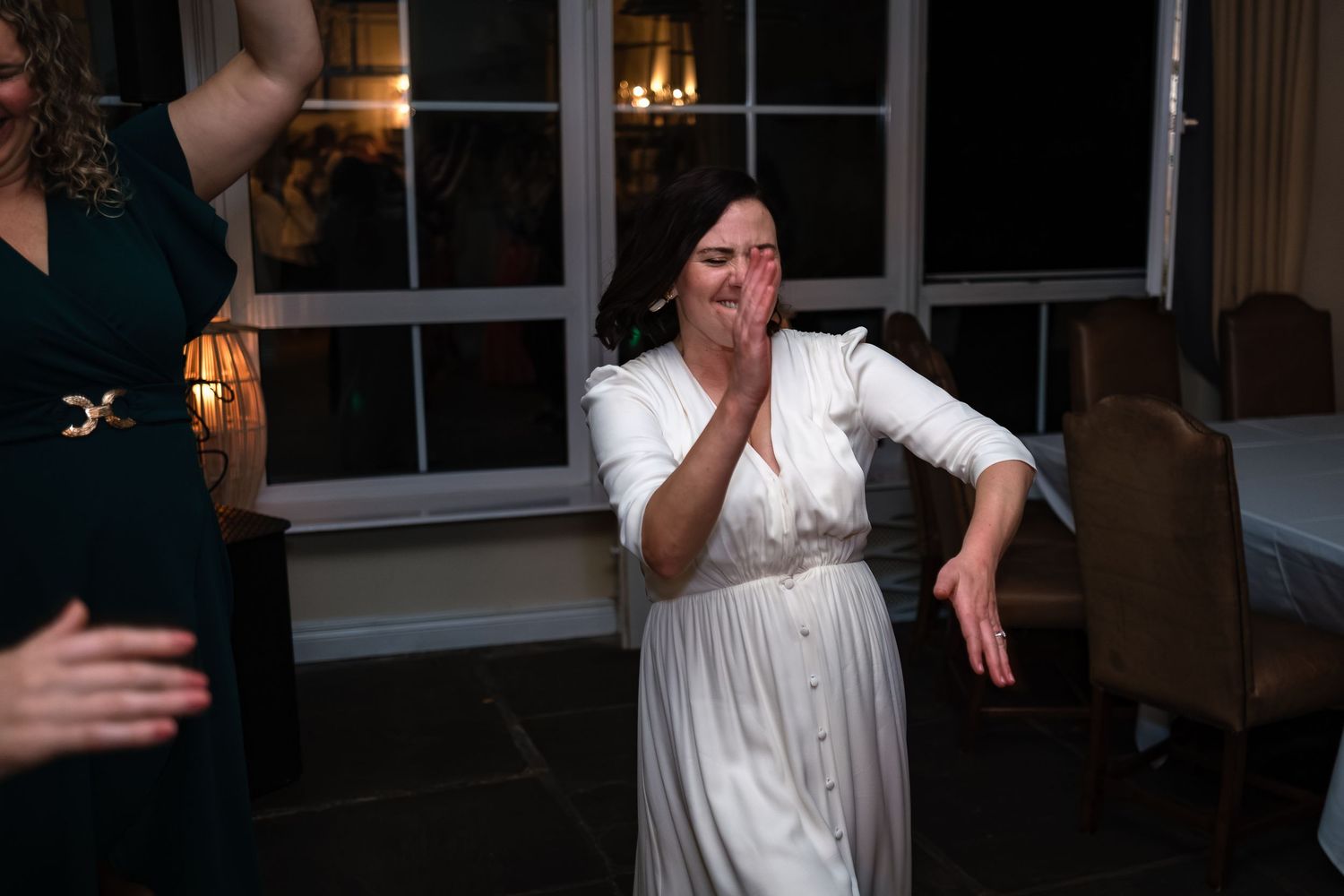 Bride in white dress laughing with hand over mouth while dancing at her wedding reception.