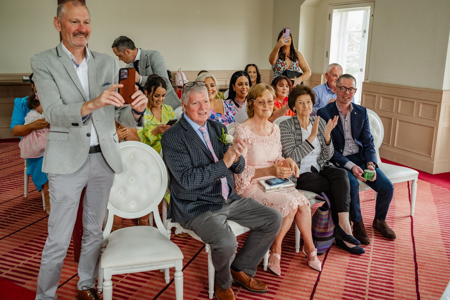 Wedding guests sitting together in formal attire during an indoor celebration.