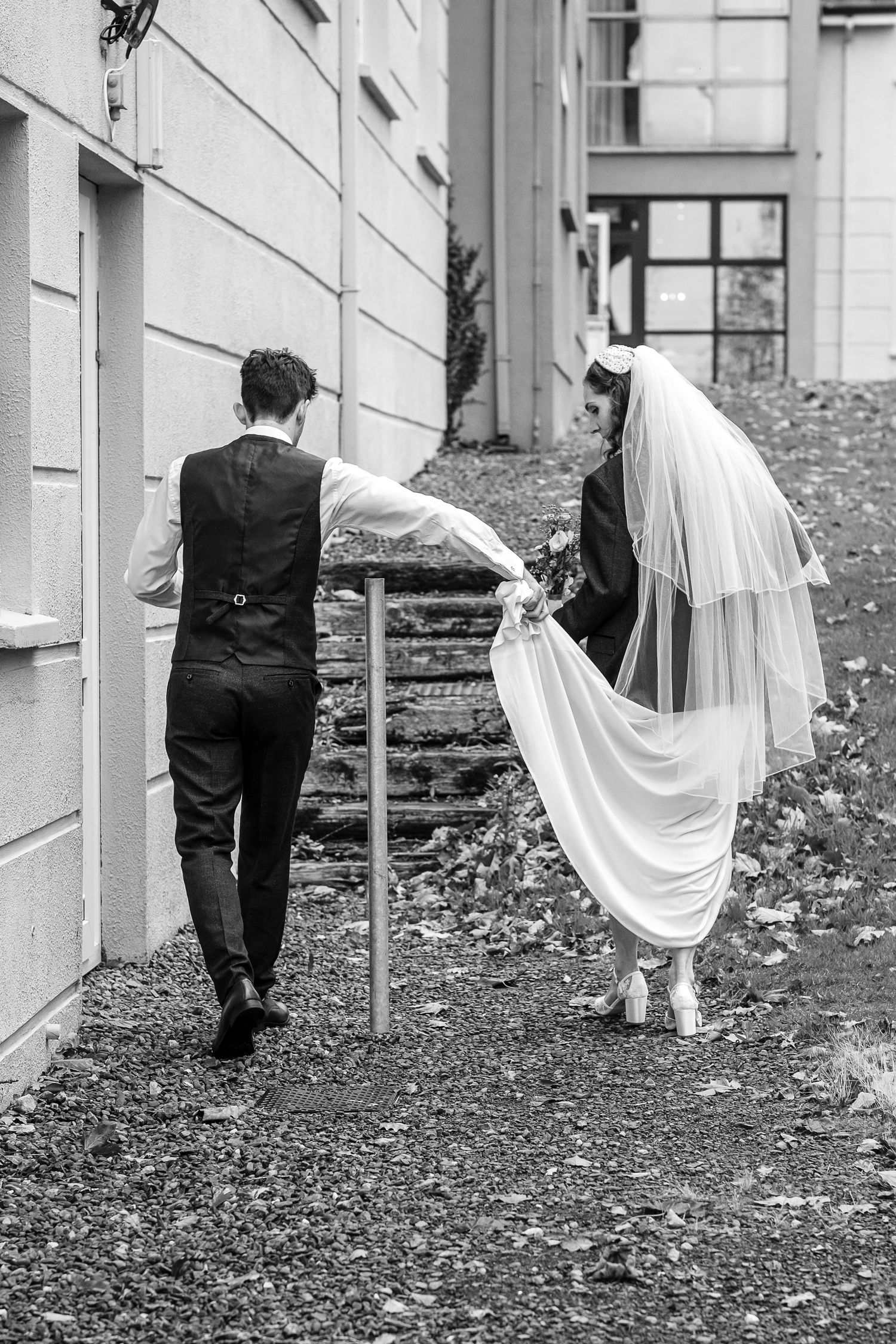 Black and white wedding sequence showing couple walking playfully through leaves beside a building.