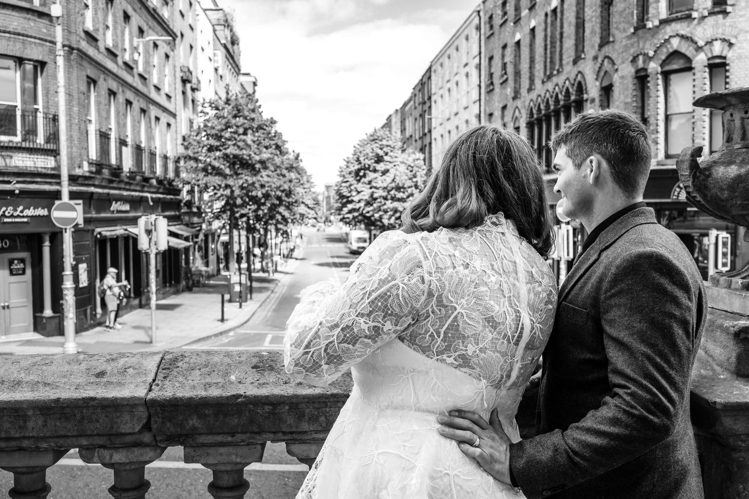 A romantic black and white cityscape view showing a couple in wedding attire overlooking an urban street.