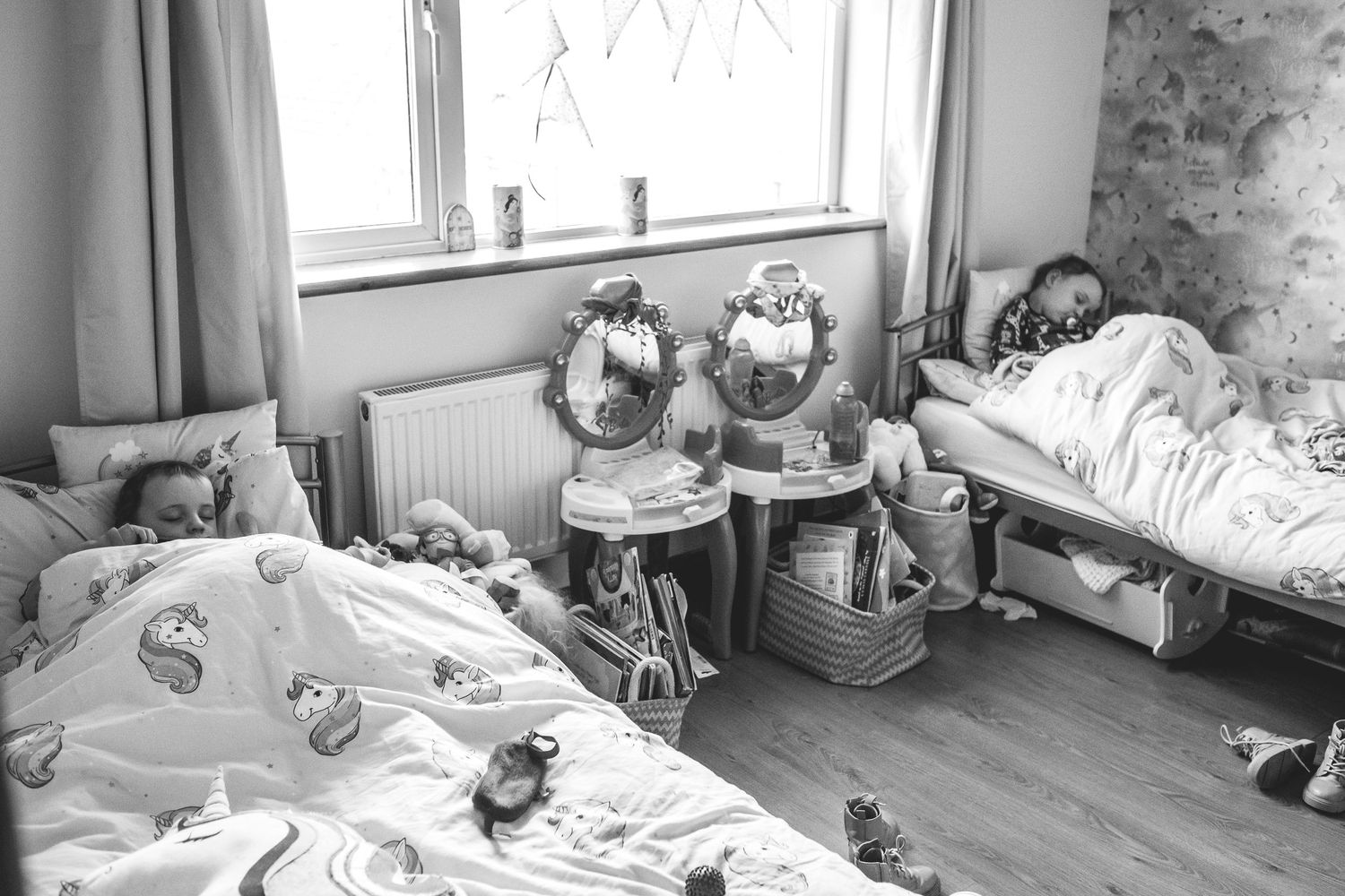 A monochrome view of an empty bedroom with twin beds and decorative items on the windowsill.