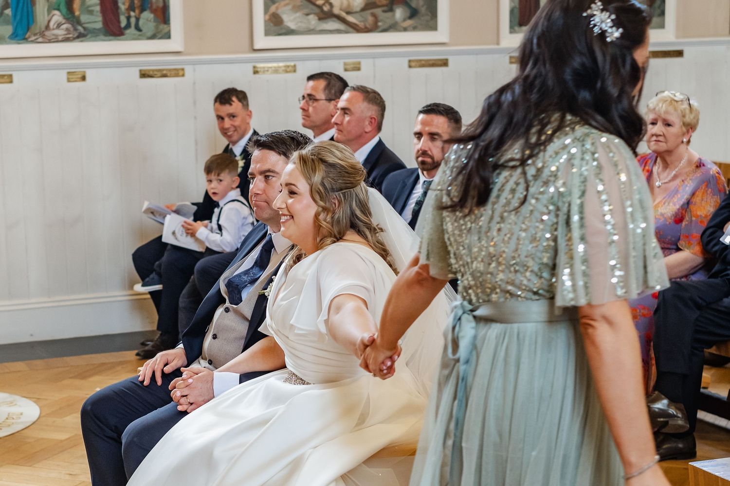 Wedding guests sharing a lighthearted moment during the ceremony in an ornate venue.