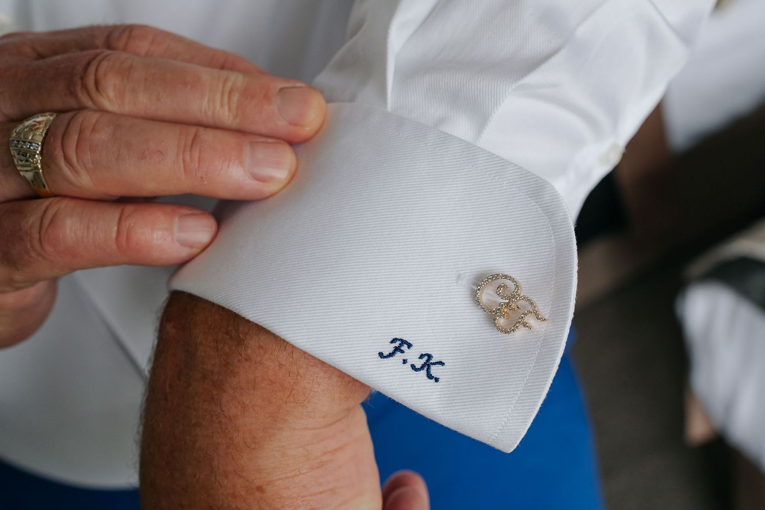 Close-up of monogrammed F.K. white dress shirt cufflinks being fastened, elegant wedding accessories detail.