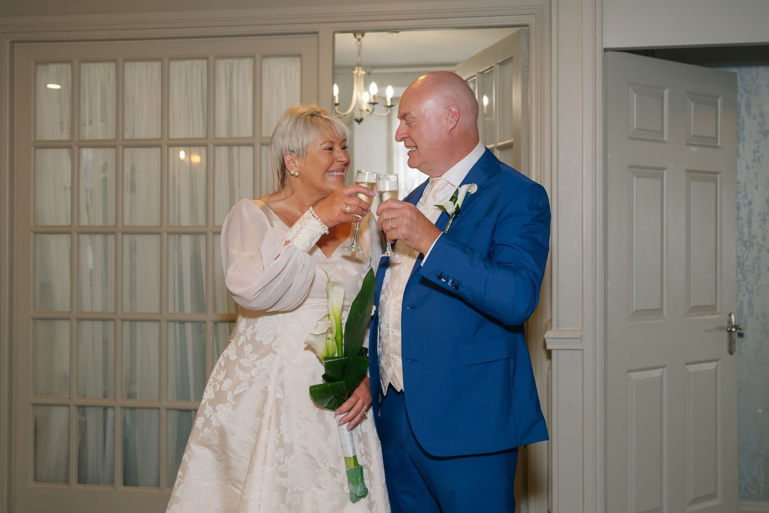 Newlywed mature couple toasting with champagne glasses after wedding ceremony indoors.