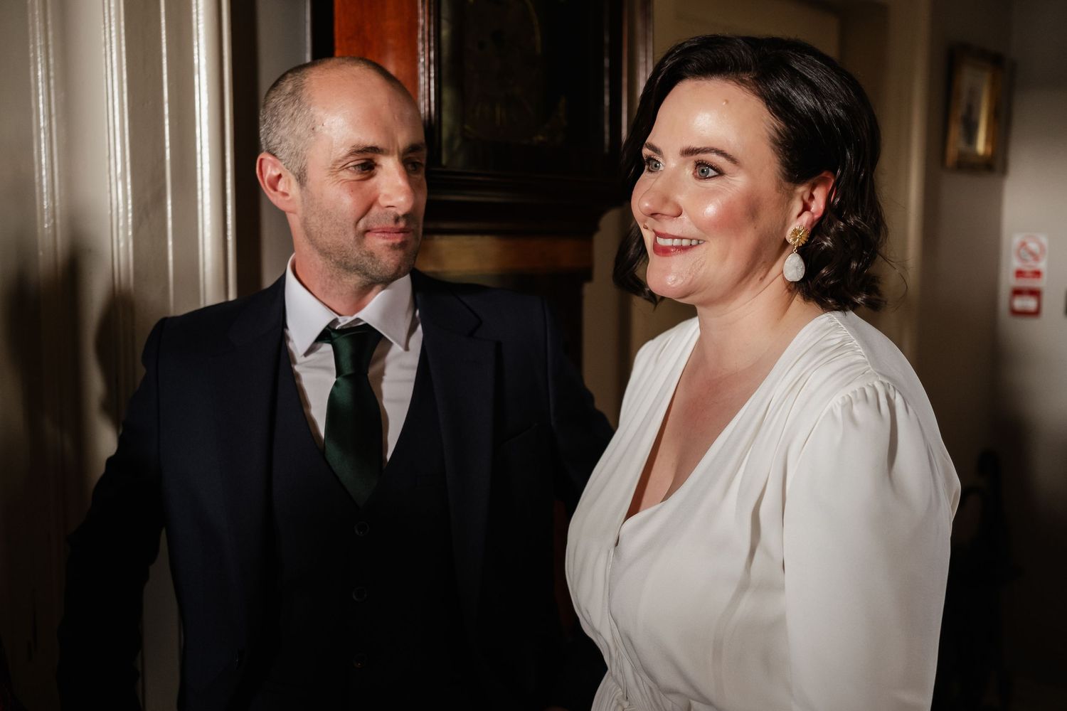 Elegant couple posing together at a formal event, man in dark suit with tie, woman in white dress smiling warmly.