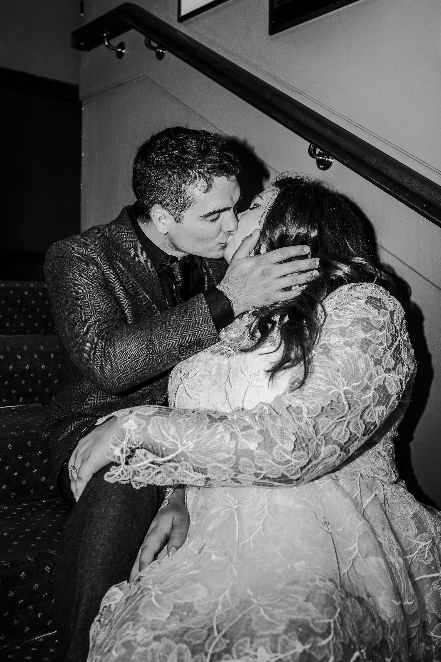 Black and white intimate moment captured on staircase with dramatic lighting.