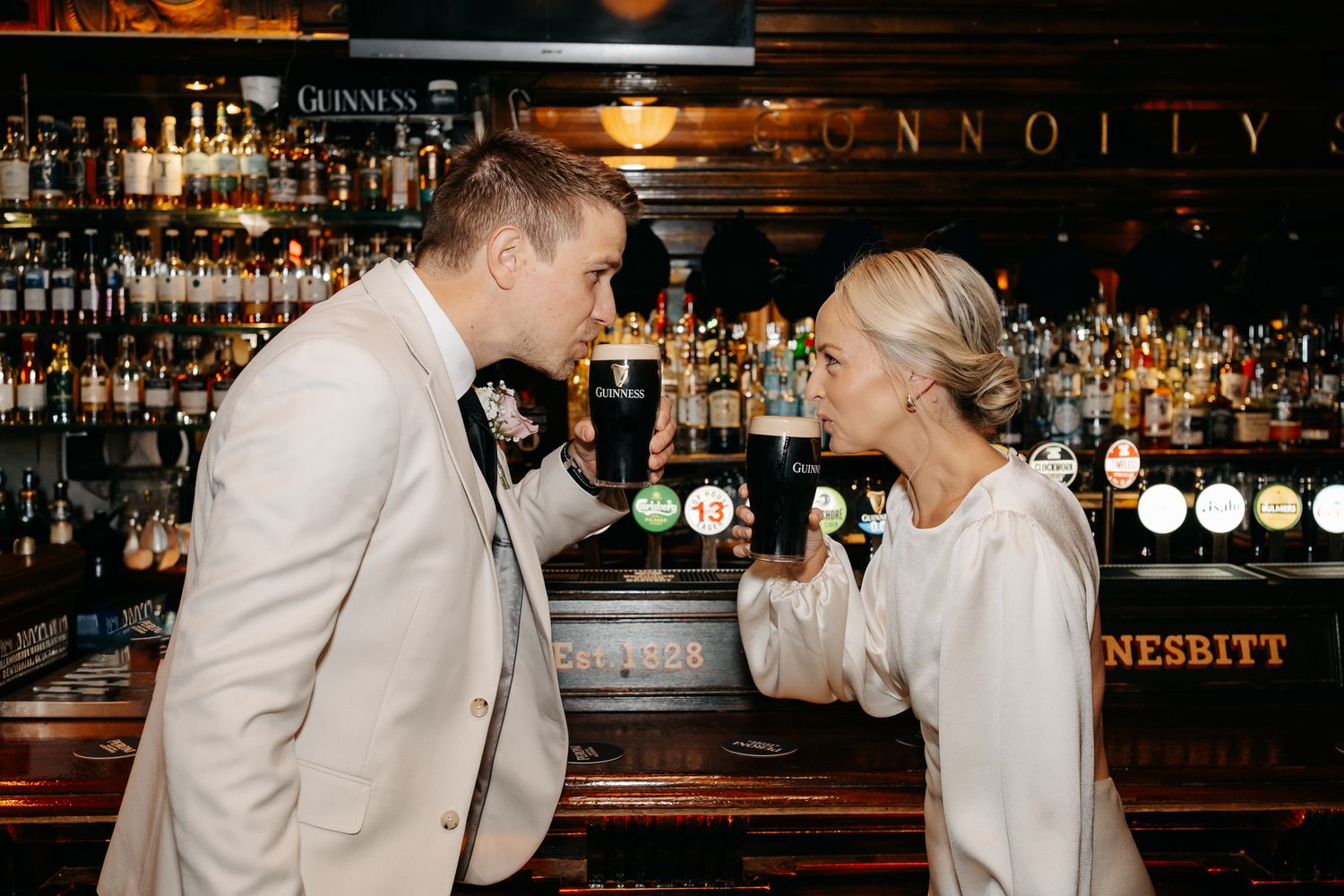 Bride and groom toasting with Guinness pints at an Irish pub bar on their wedding day.