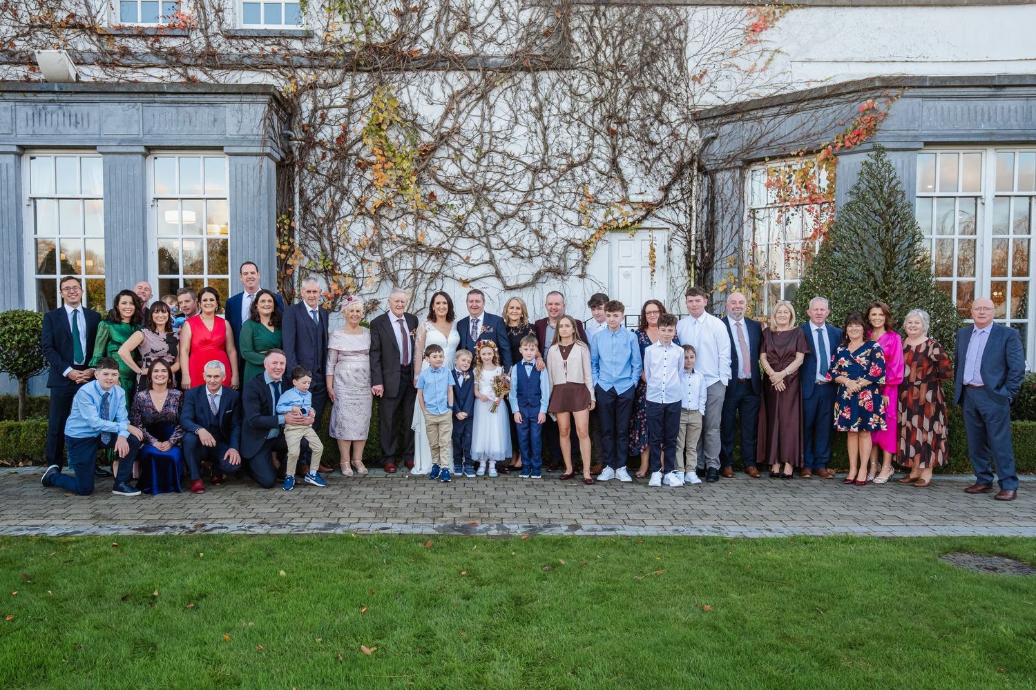 Large family group portrait outdoors in front of an elegant building, gathered for a special occasion.