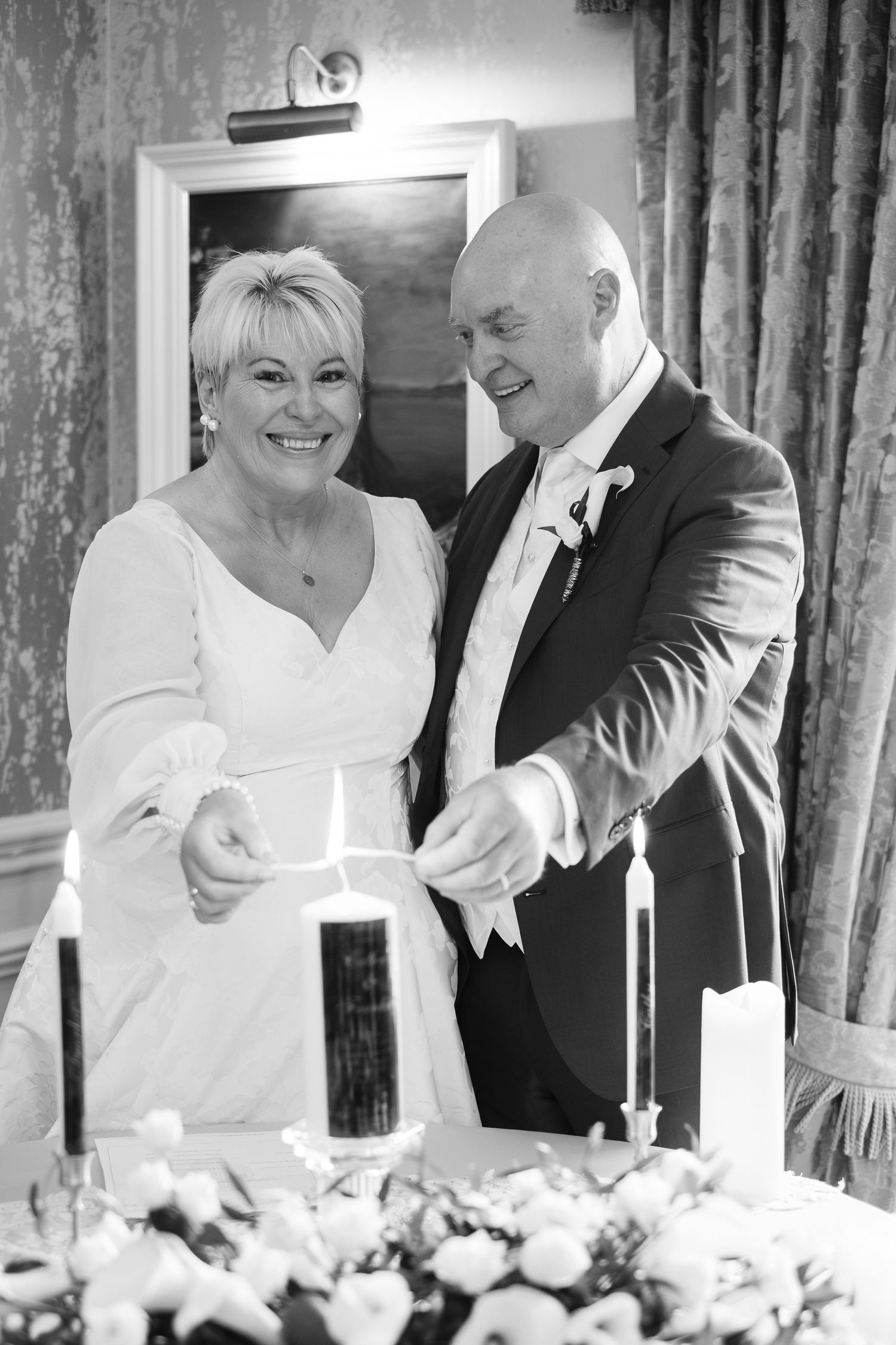Bride and groom lighting unity candle together at wedding ceremony in black and white photo.