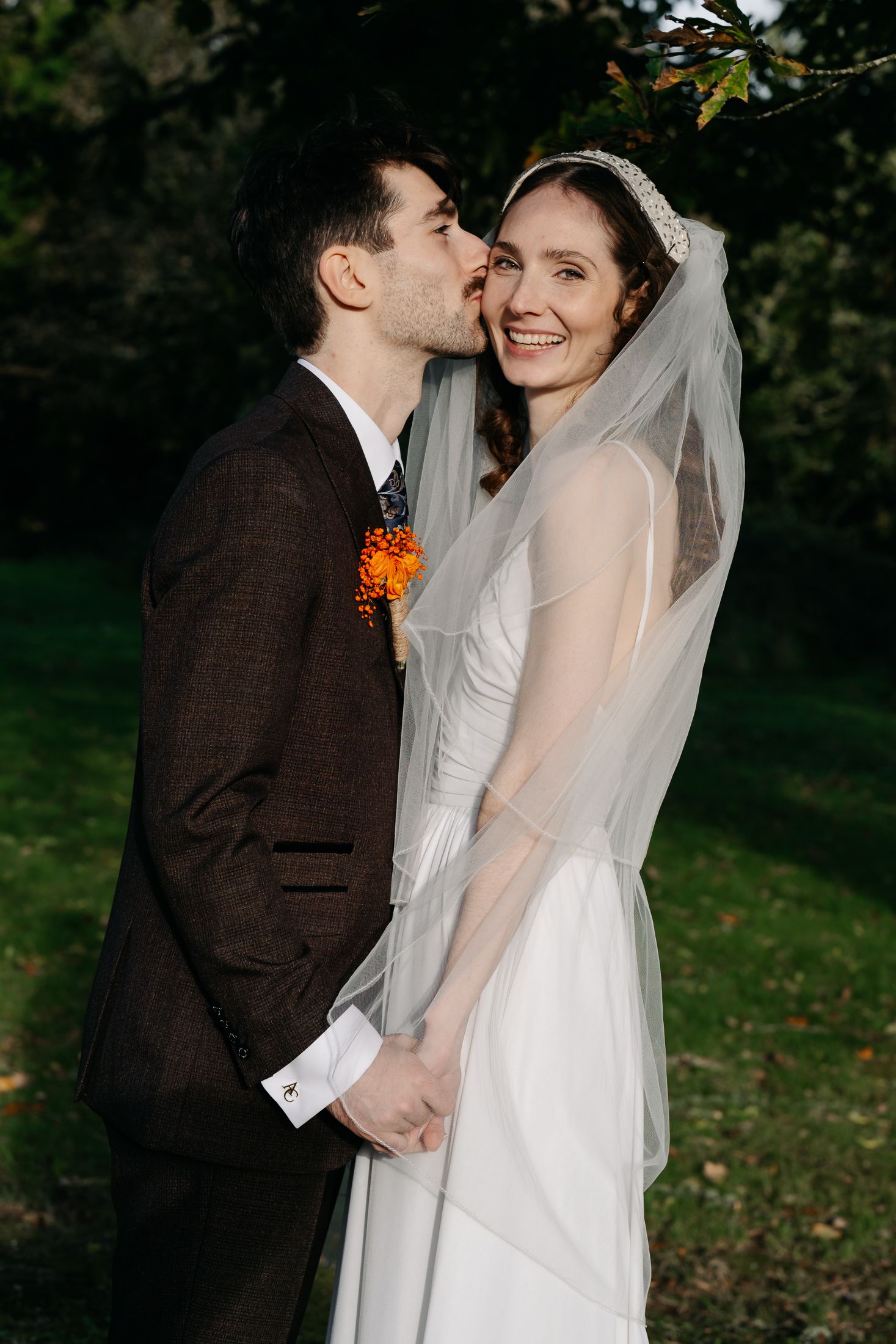 A romantic wedding couple shares a tender moment outdoors in an autumn garden setting.