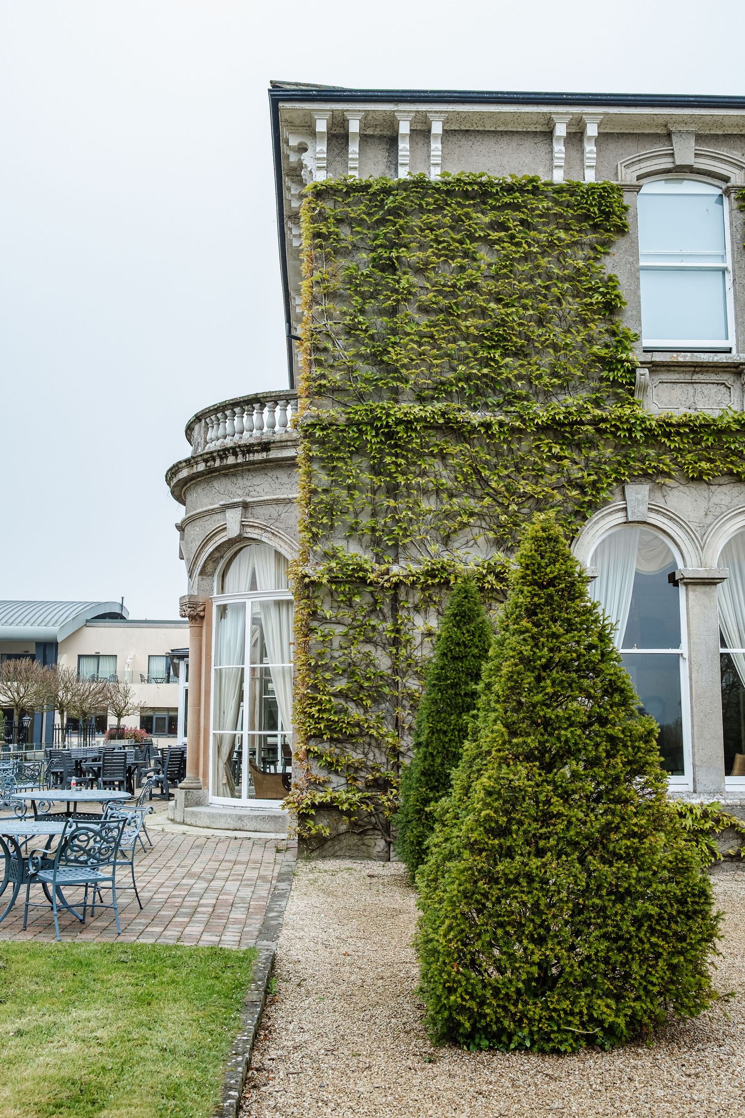 Elegant stone building exterior with ivy-covered walls and a terrace featuring outdoor seating furniture.