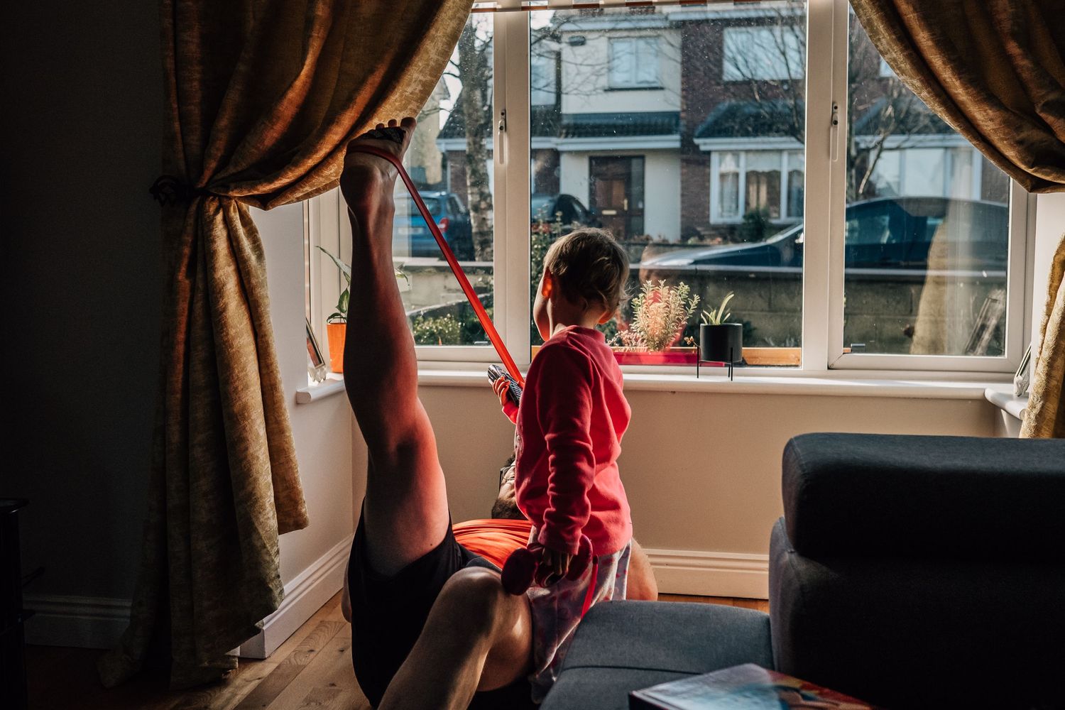 Person in red shirt sitting by window with brown curtains.