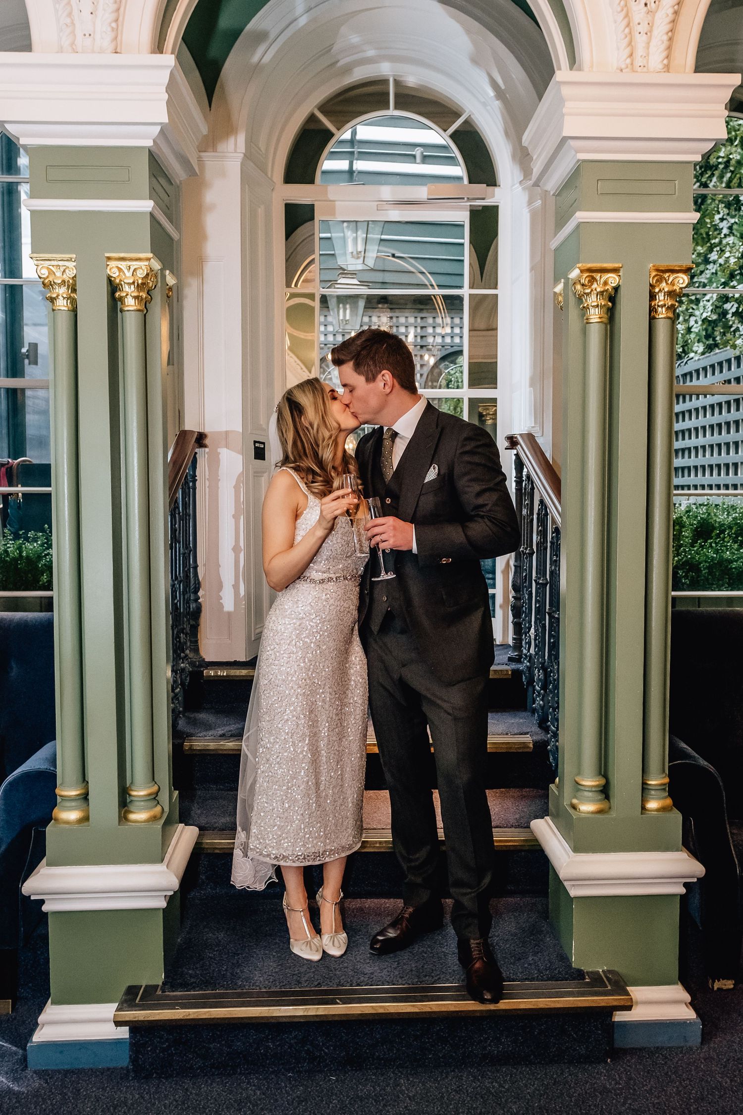 Elegant couple sharing a moment under arched columns with champagne glasses.