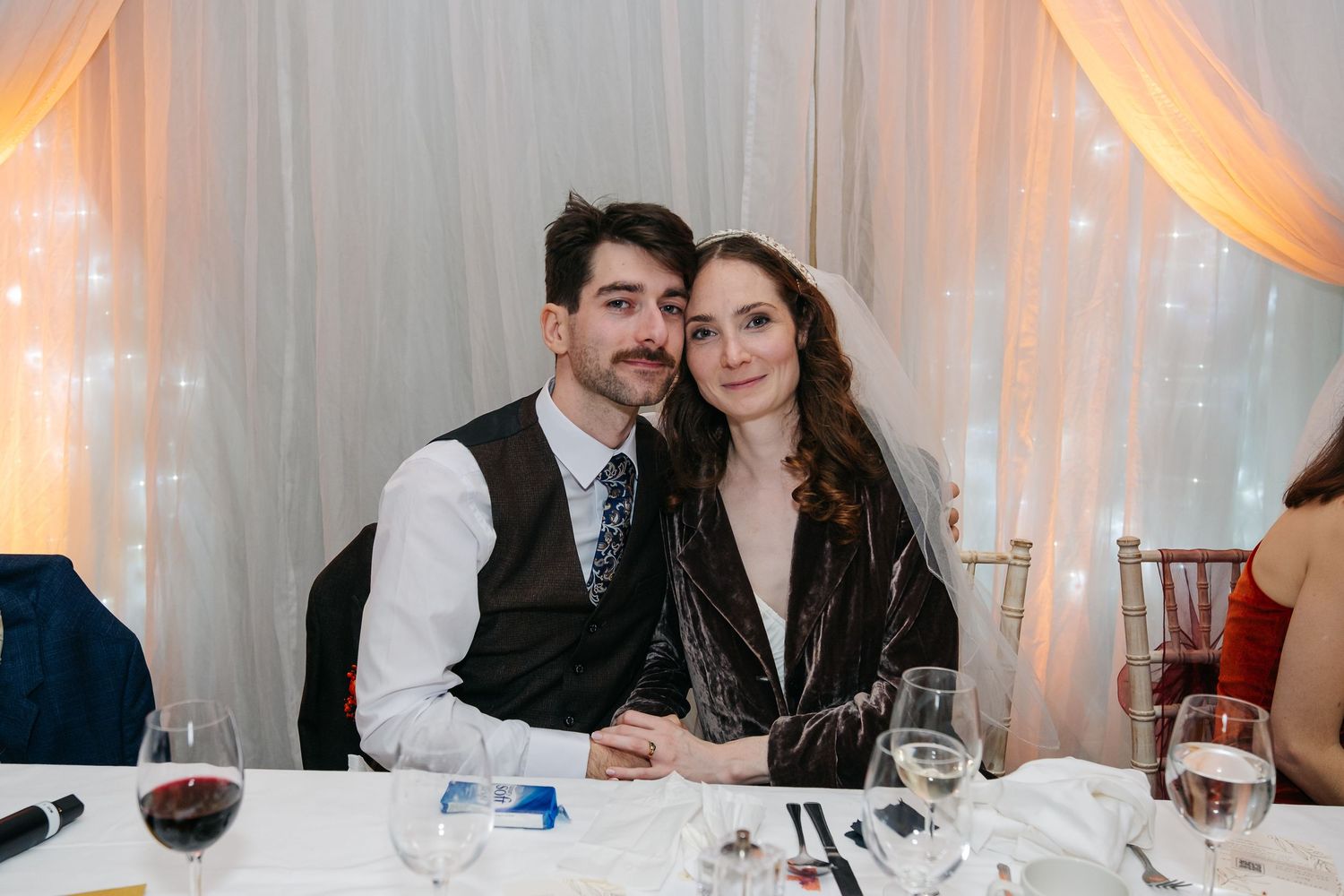 Wedding reception dinner tables decorated with warm lighting and elegant white draping.