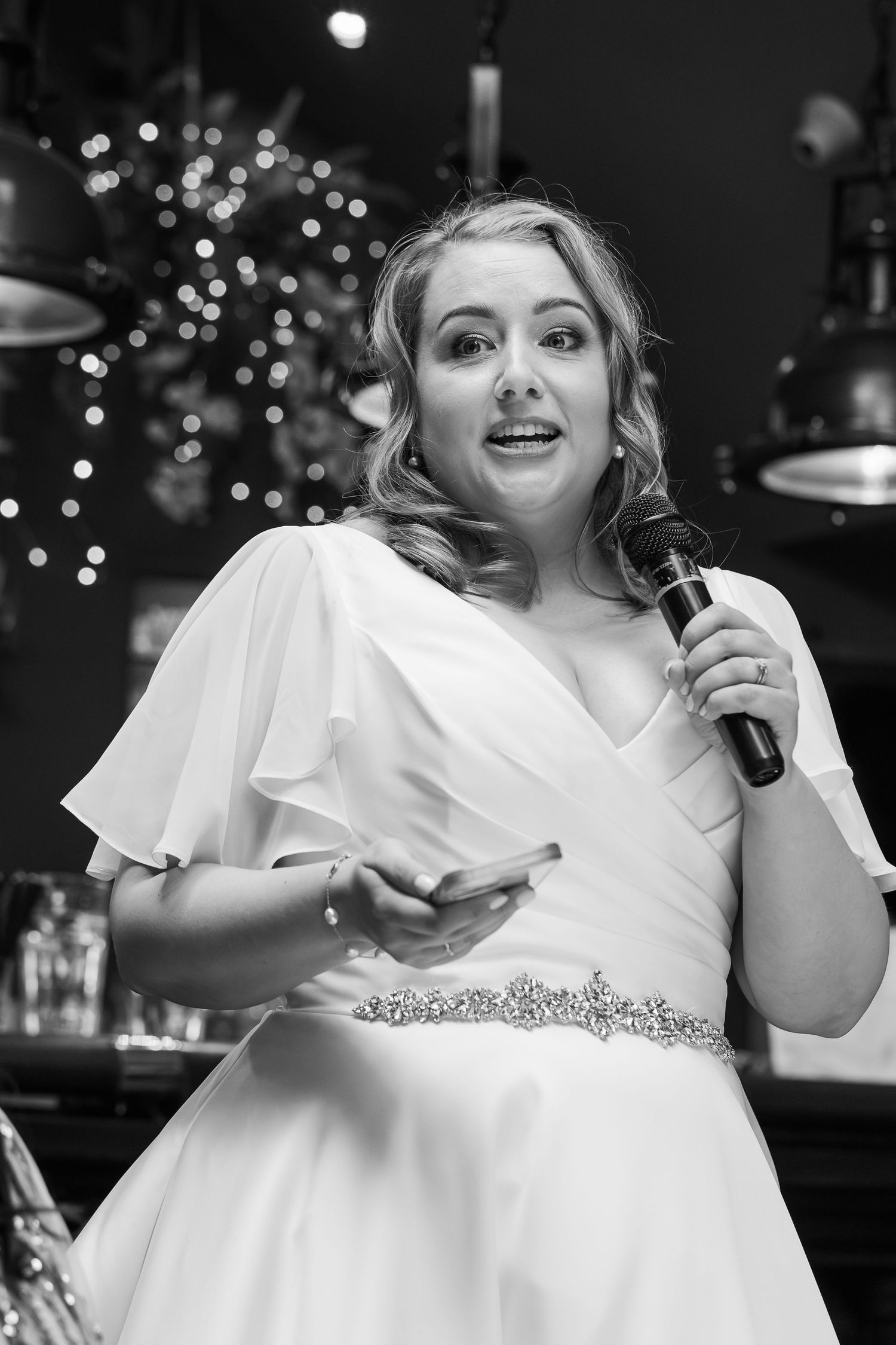 Black and white portrait of bride giving speech with microphone at wedding reception.