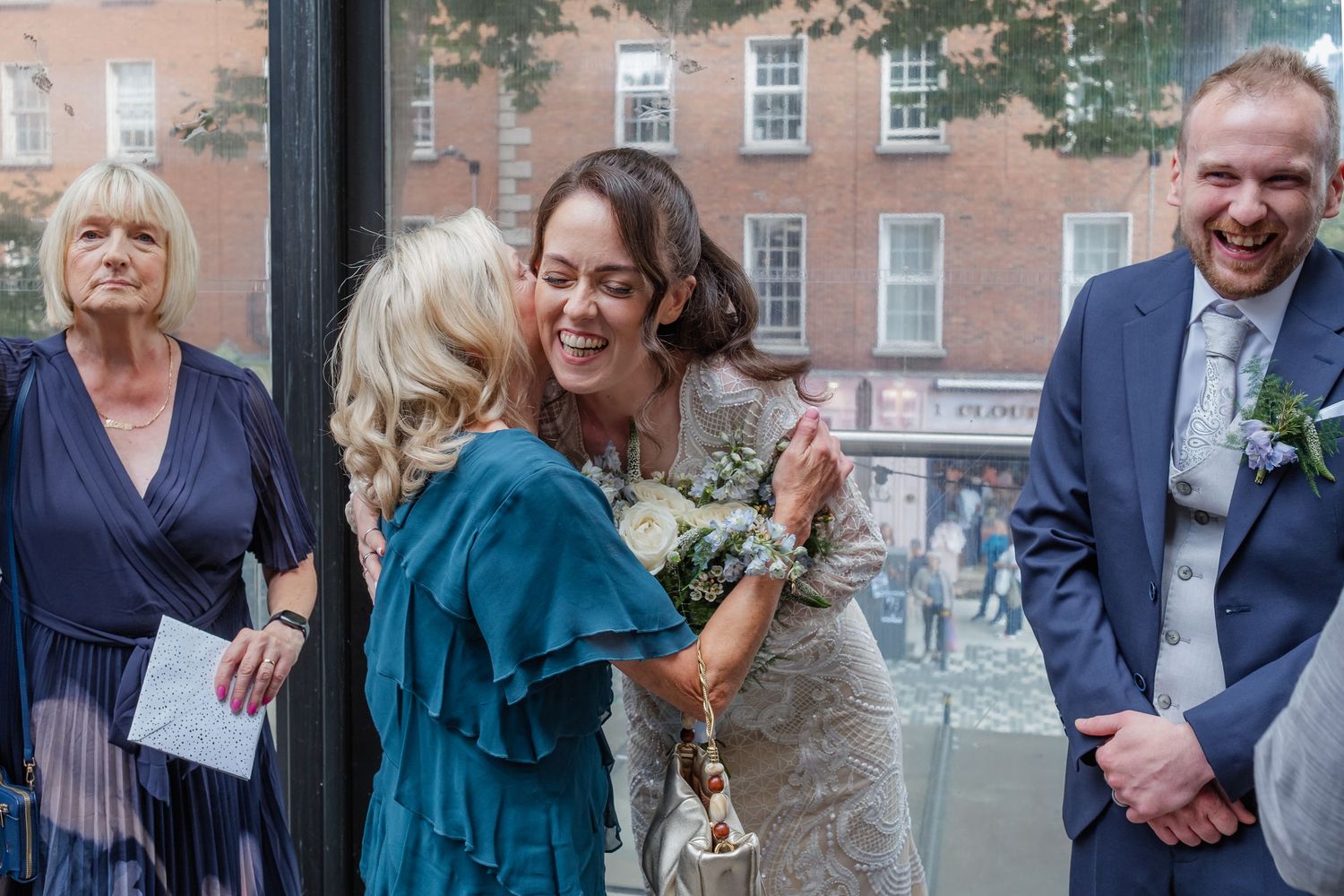 Wedding celebration with guests in formal attire gathered outside brick buildings.