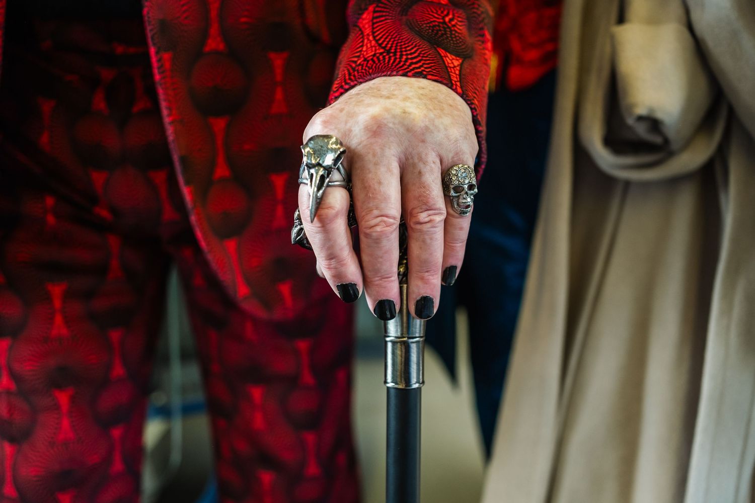 Hand wearing ornate rings holding a walking cane against red fabric.