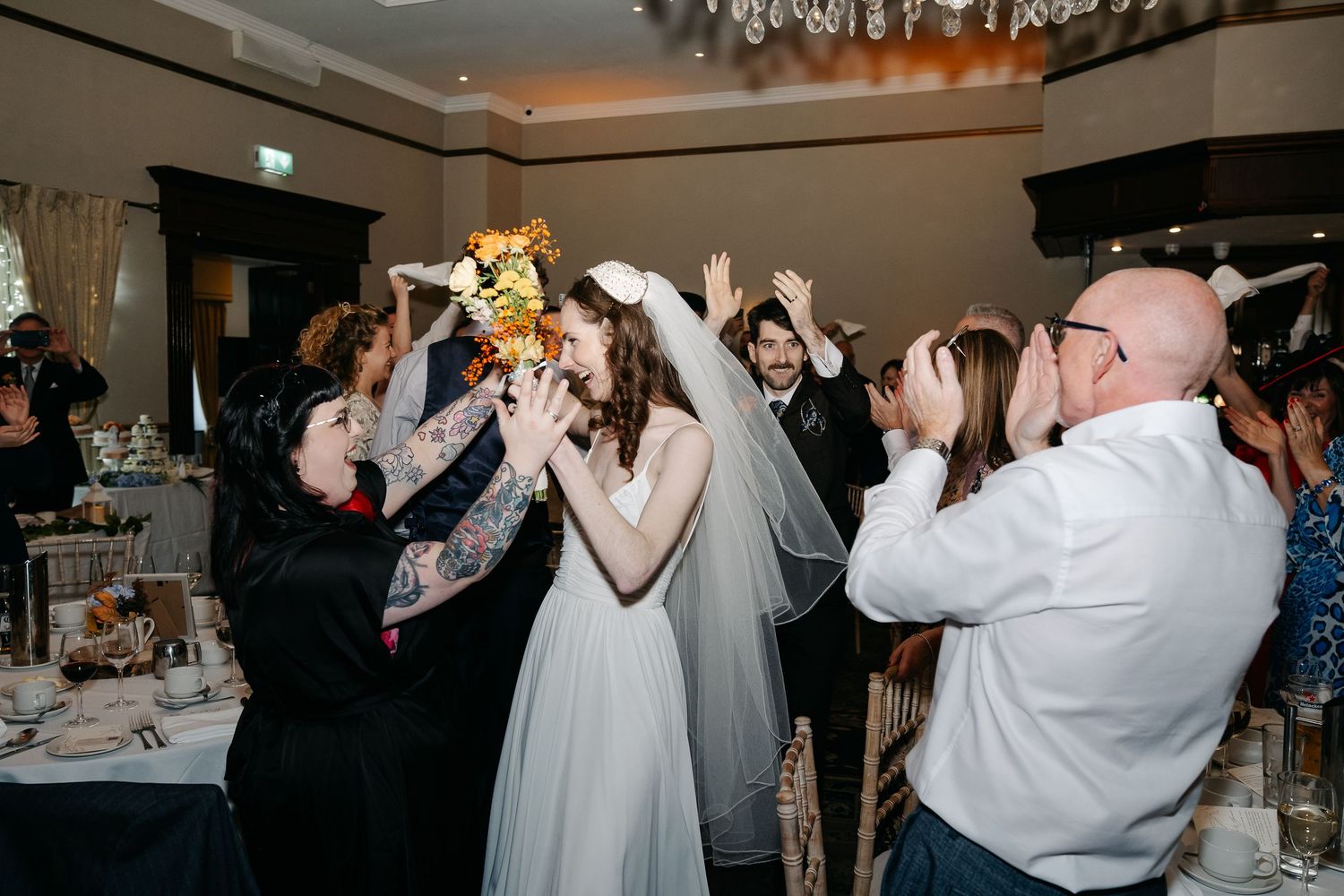 Wedding guests dancing and celebrating on a dimly lit dance floor at an indoor reception.