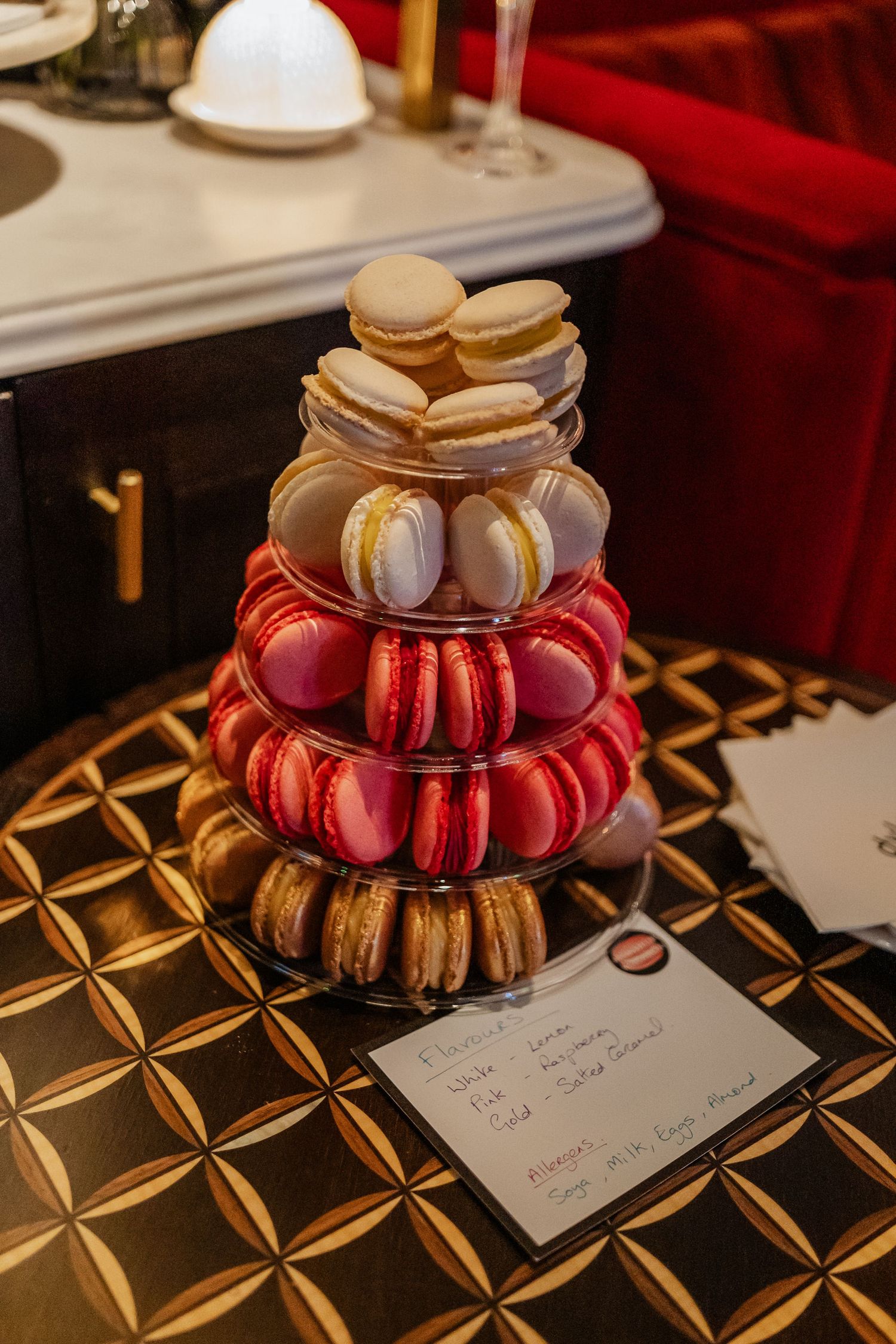 Tower of colorful macarons arranged on a gold-patterned surface with a handwritten note.