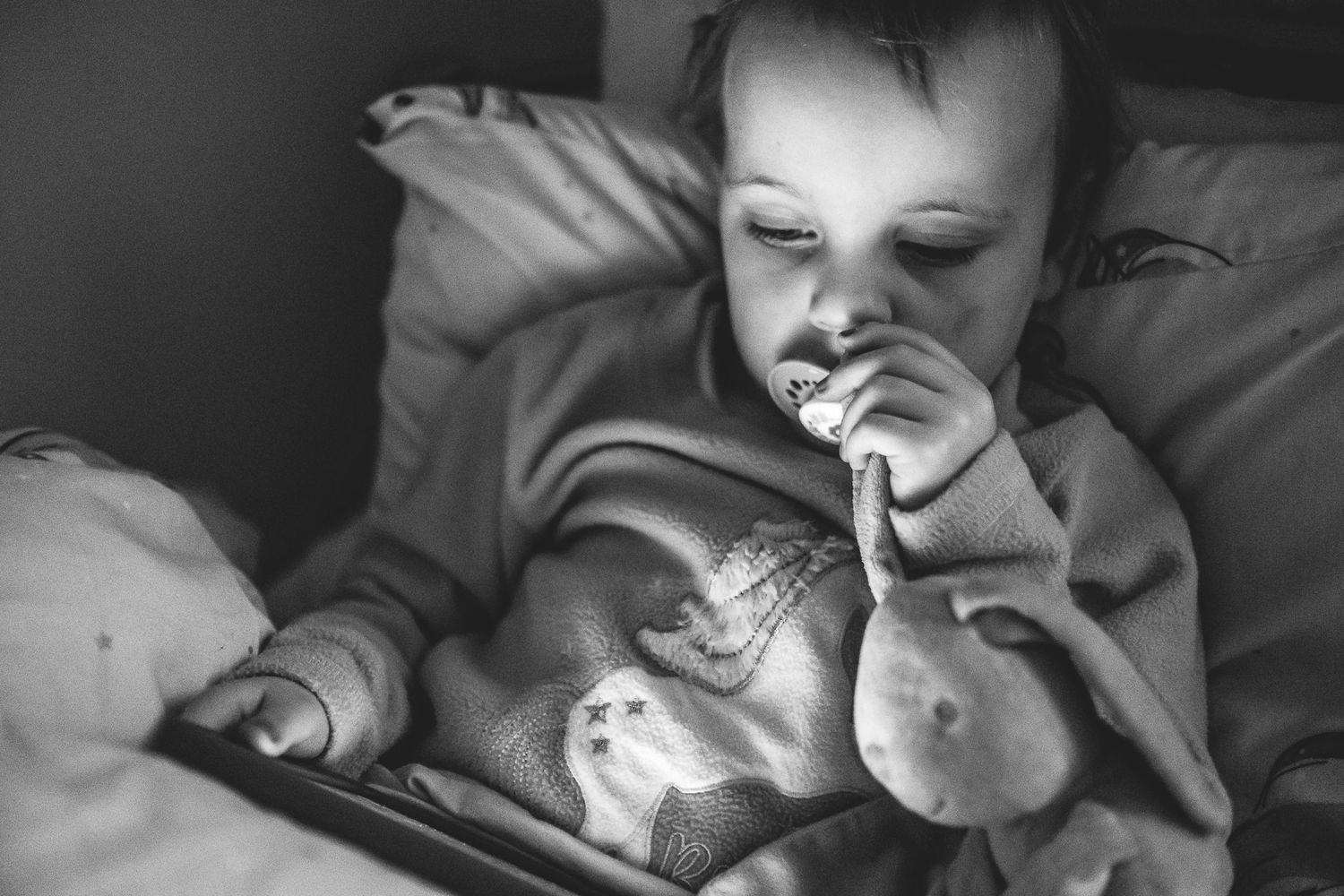 Child using a glowing tablet device while lying in bed at night.