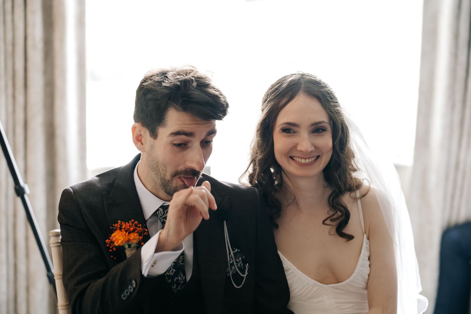 A couple shares a tender moment at their wedding, with the groom kissing the bride's hand in a sunlit room.