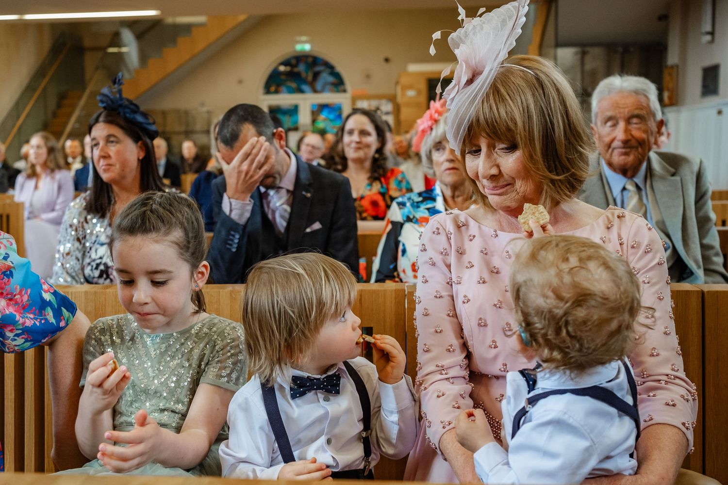 Young children in formal attire sit together at church pews during a wedding ceremony.