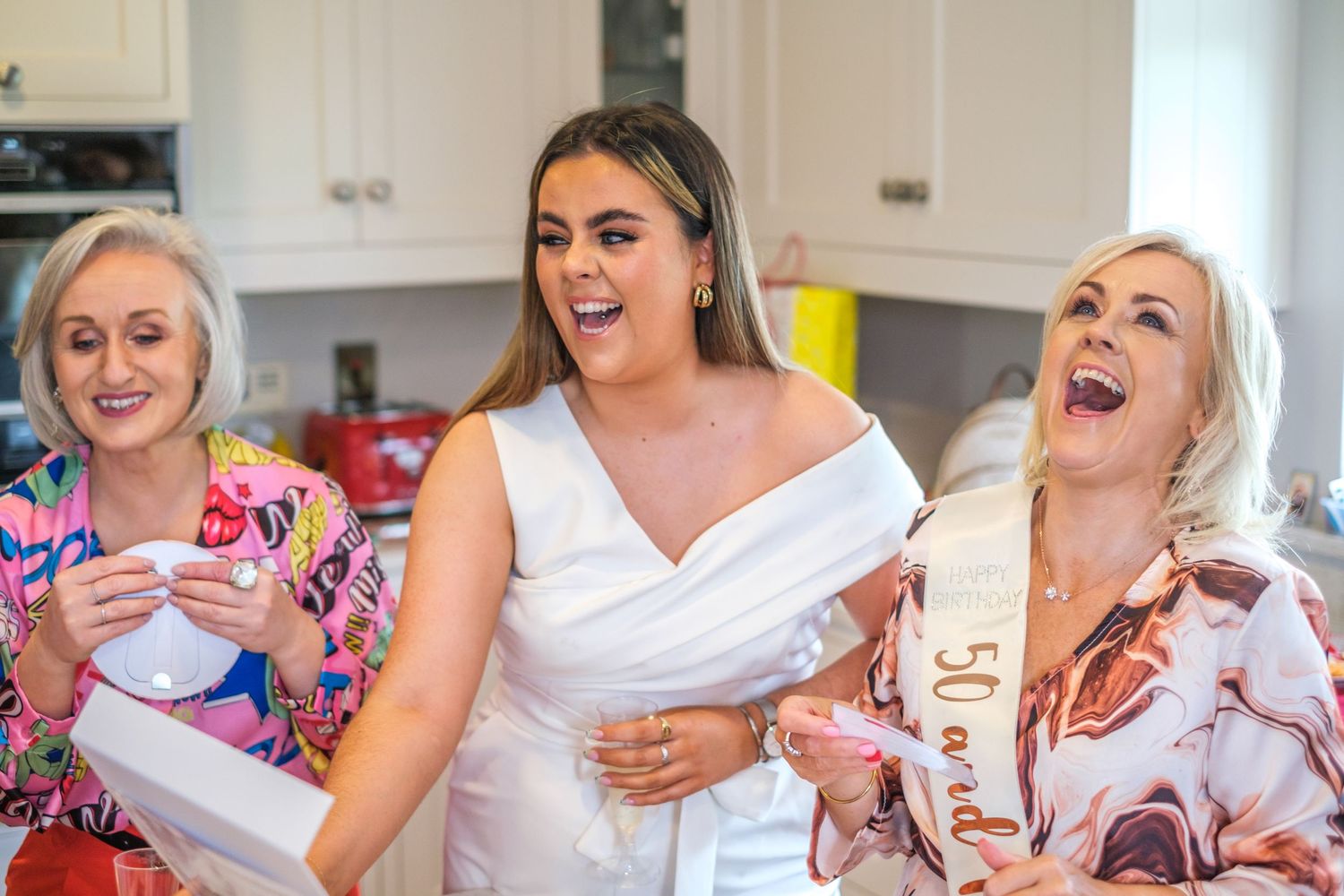 A group of people in white tops sit together laughing and enjoying beverages during a social gathering.