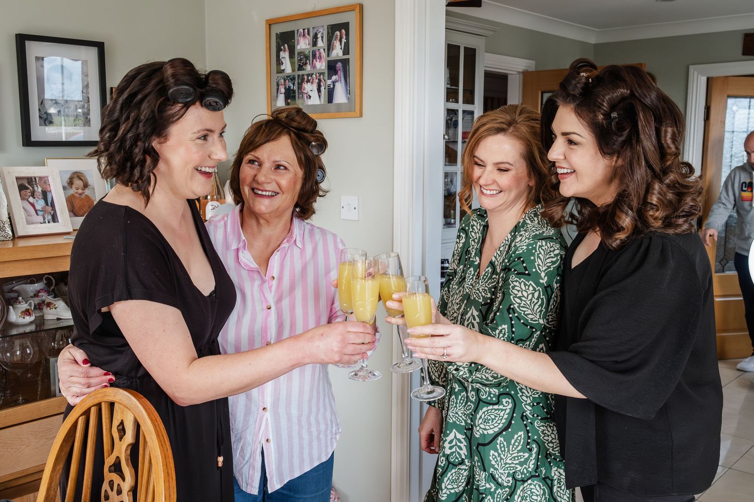 Four women smiling and toasting with champagne glasses at a cheerful indoor celebration.