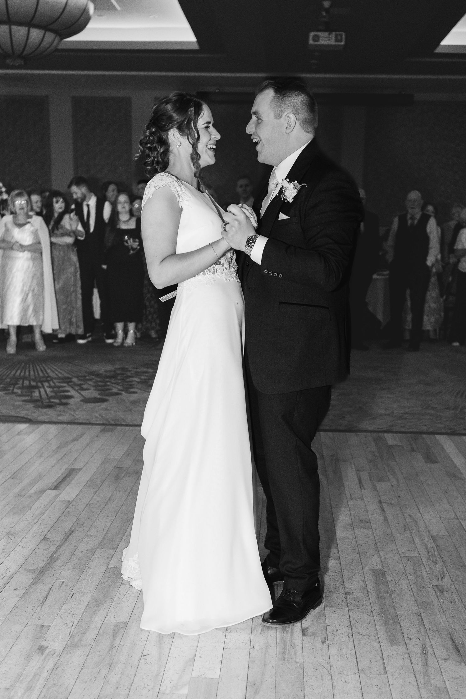 A couple shares a romantic dance moment on a wooden floor at what appears to be a wedding reception.