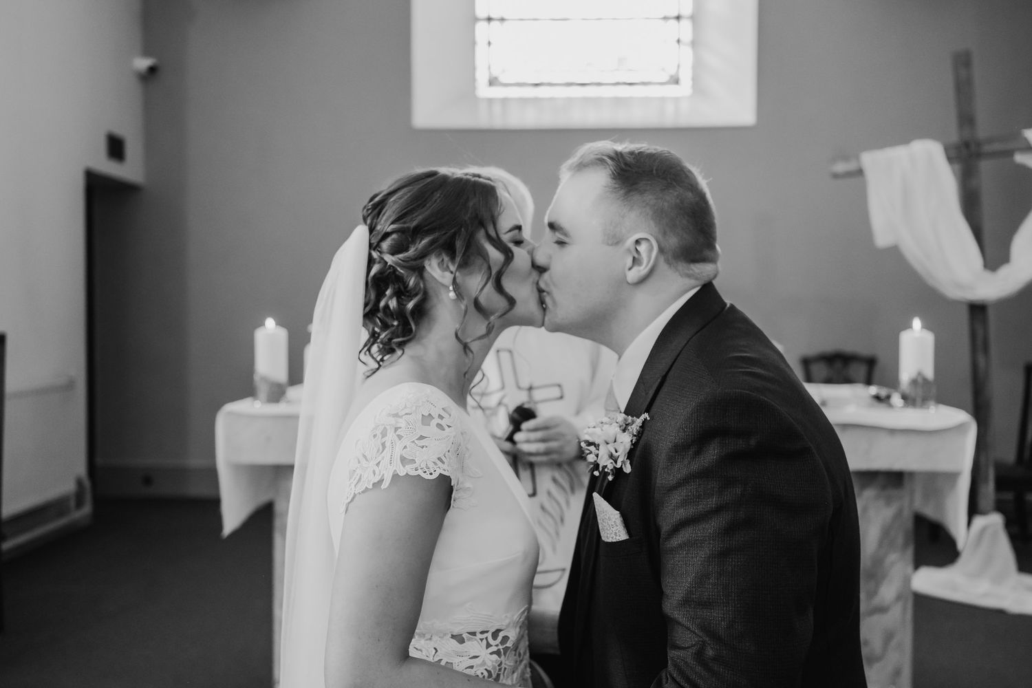 A black and white wedding ceremony photo showing an intimate moment between newlyweds in a church setting.