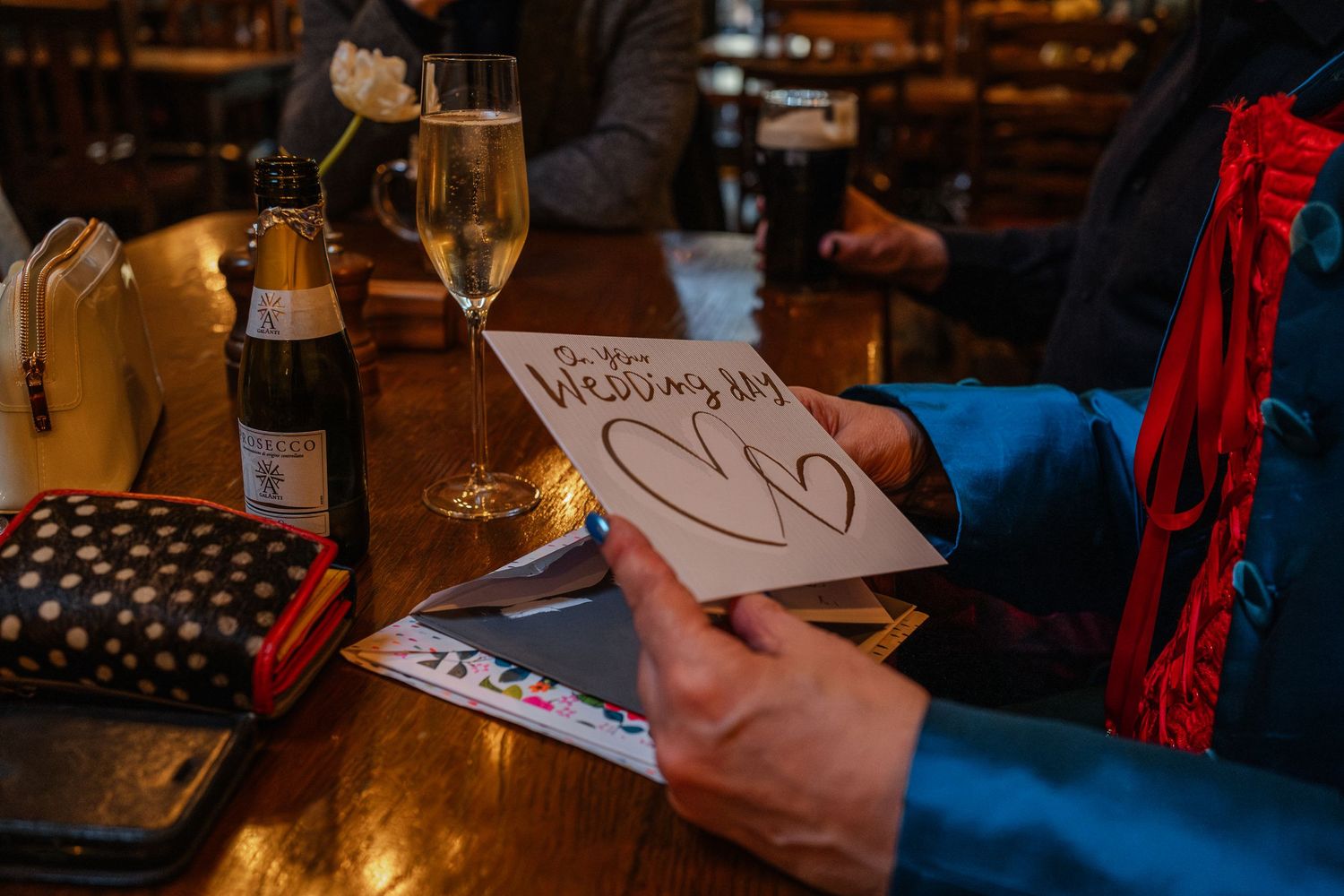 Hand holding a pen writing on paper with drinks and wine glasses on table.