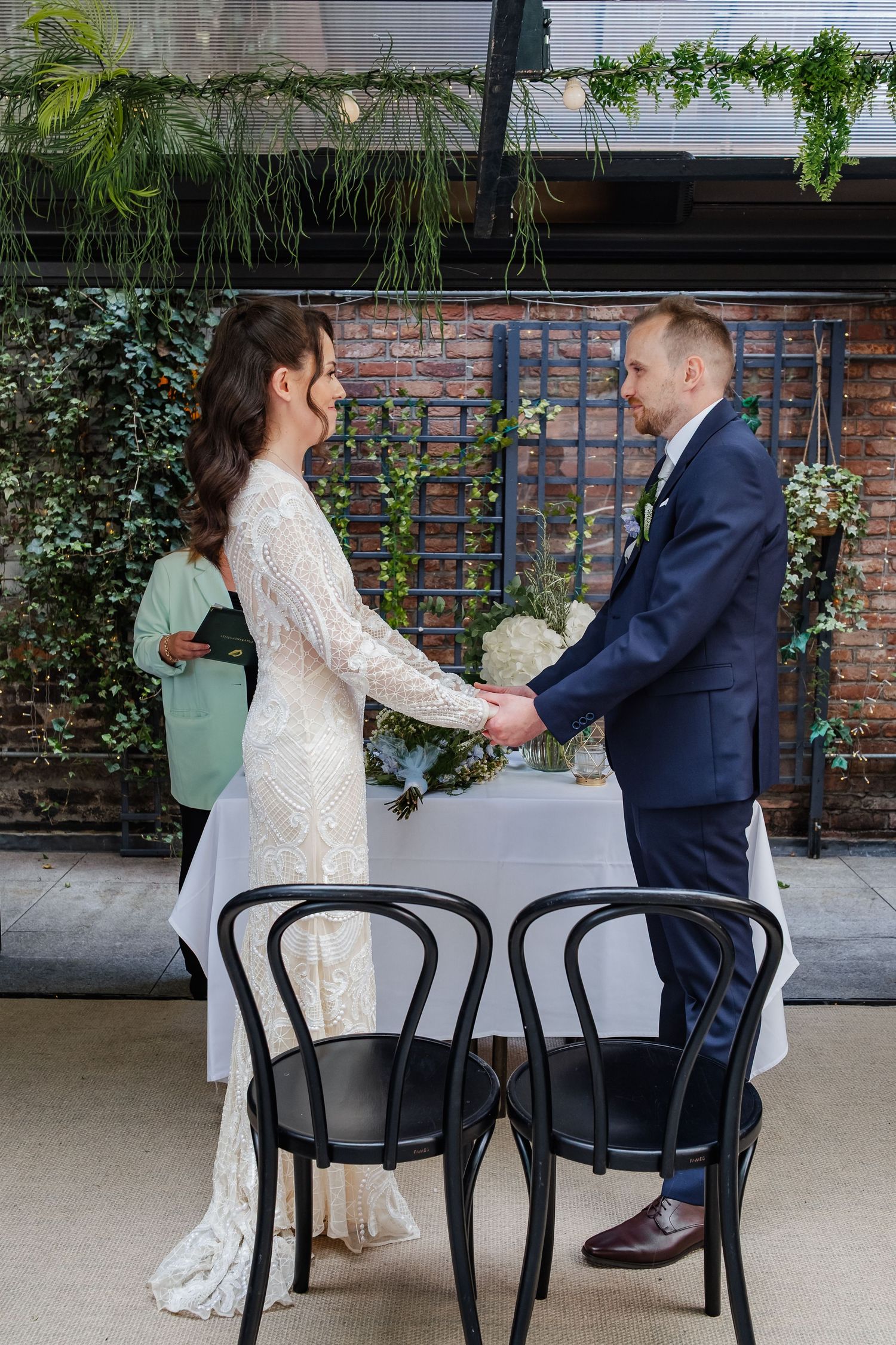 Wedding ceremony in an industrial-chic venue with brick walls and hanging greenery.