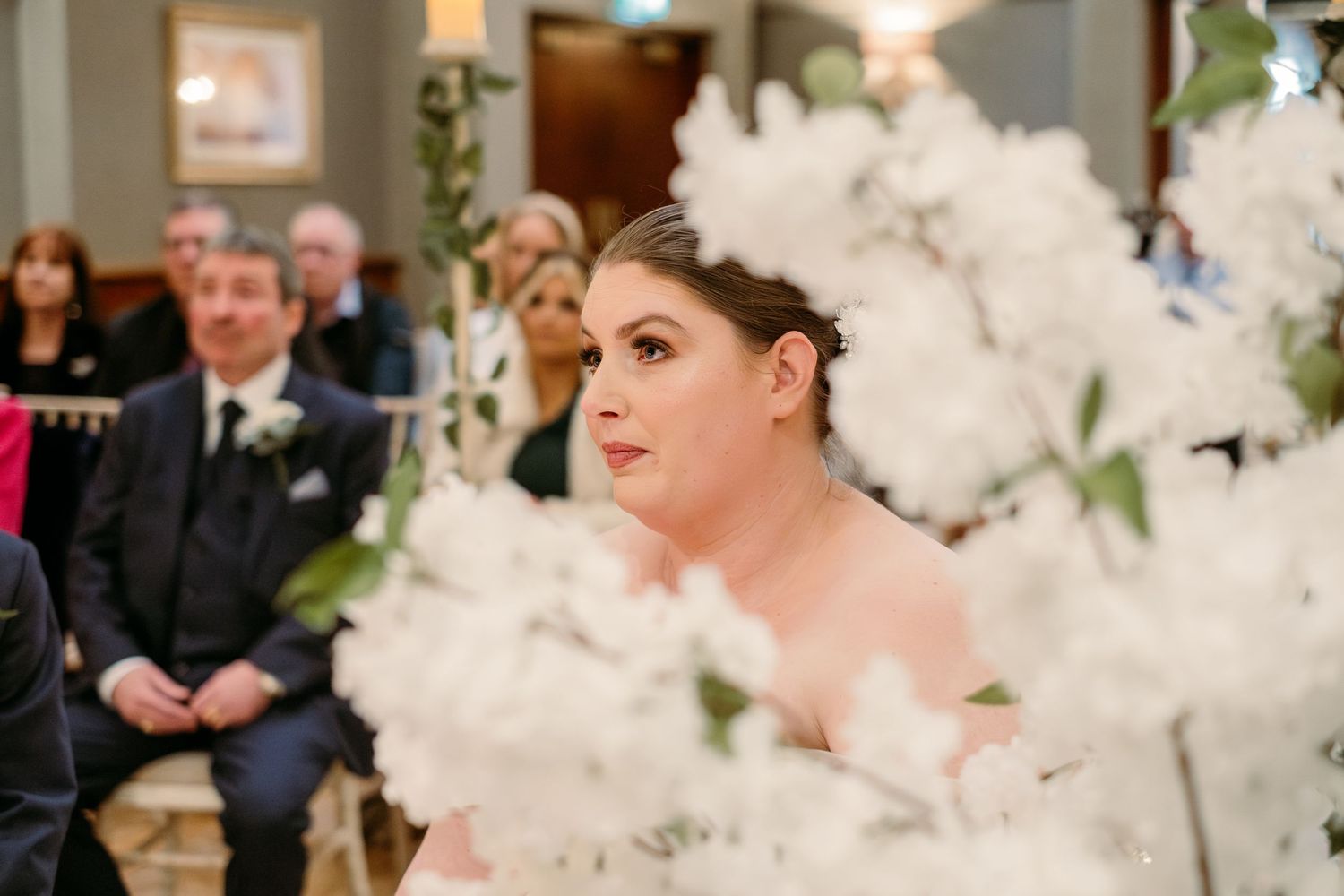 A wedding ceremony scene with dramatic white floral decorations in an elegant indoor setting.