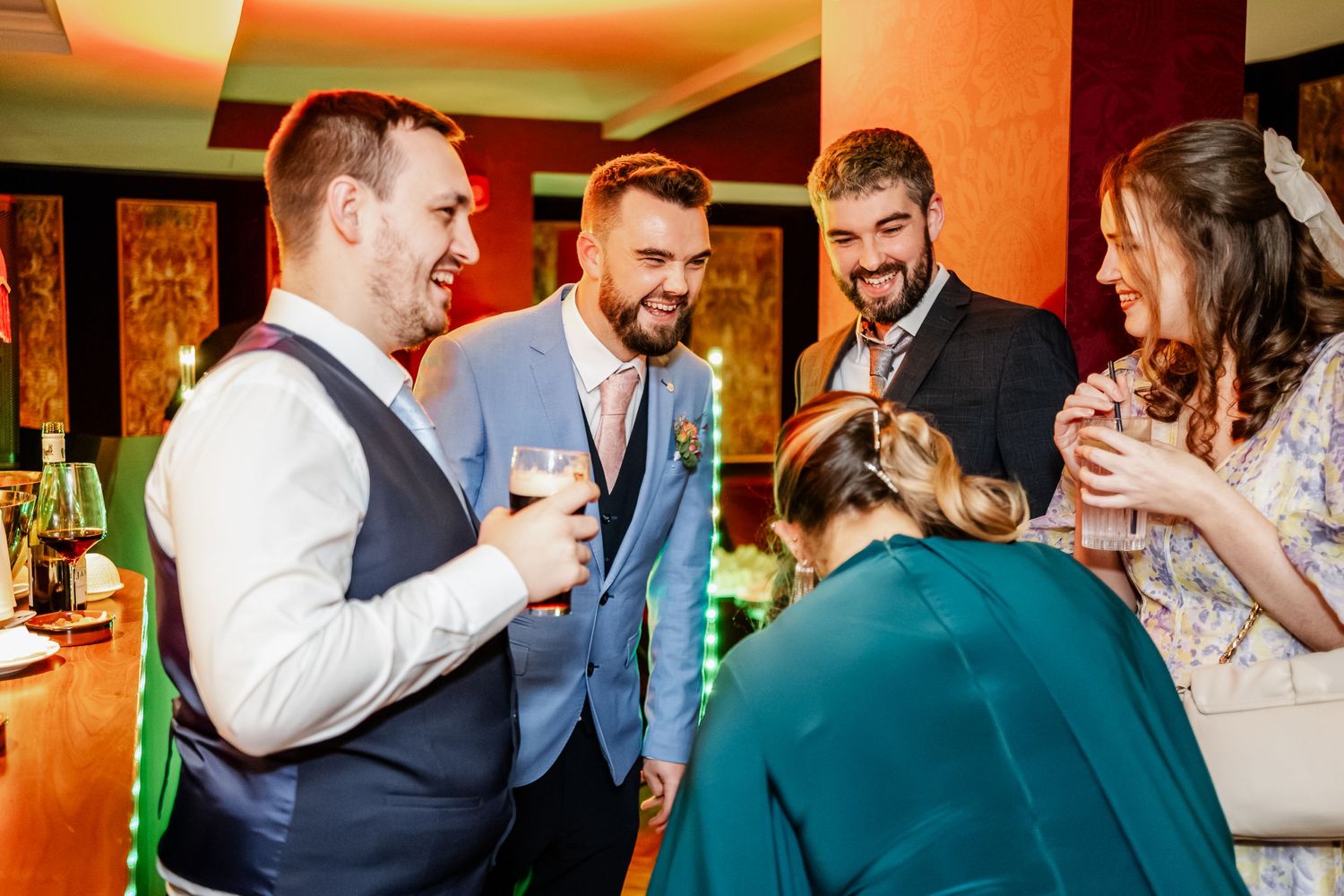 Wedding guests sharing drinks and laughter during a reception celebration.