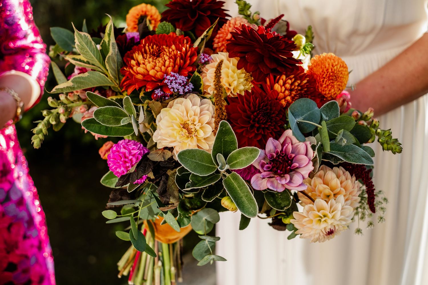 Stunning autumn wedding bouquet featuring red dahlias, orange flowers, and lush greenery.
