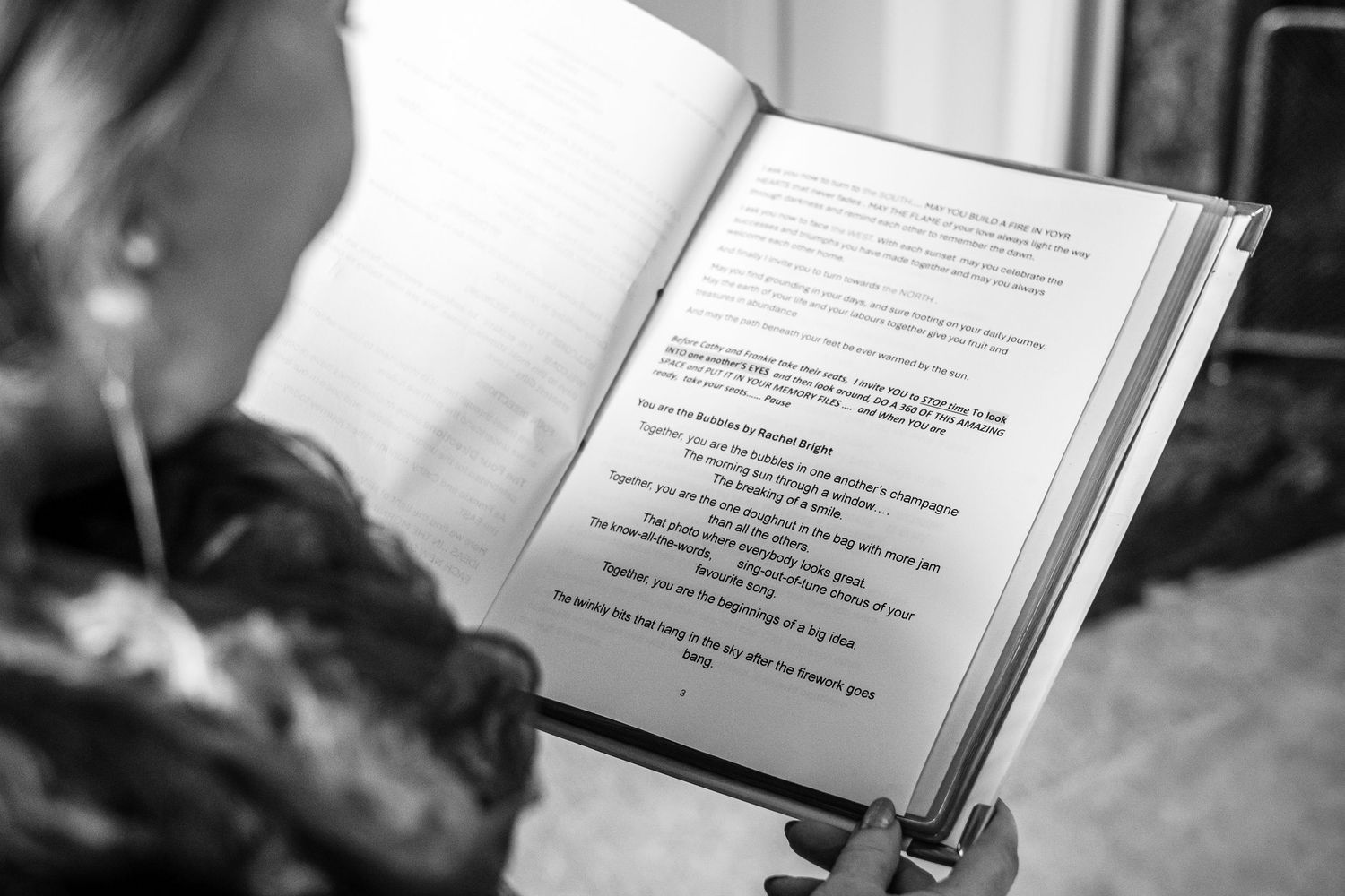 Black and white photo of officiant reading wedding ceremony vows from decorative book.