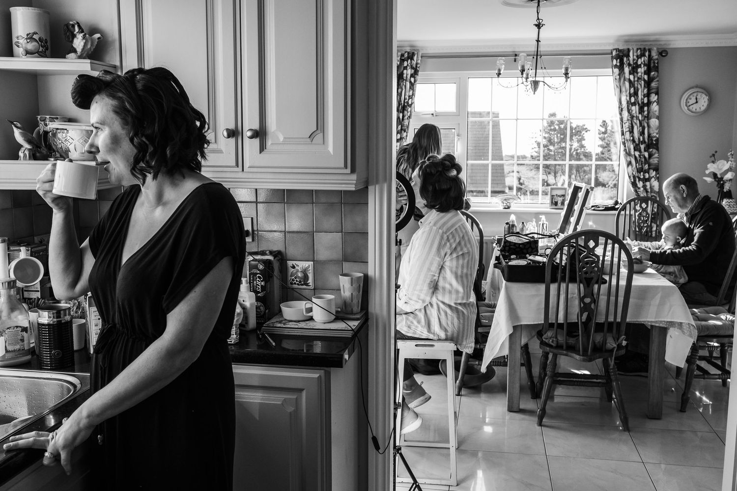 Black and white photo of women in a kitchen and dining area, one sipping coffee while others sit at a table.