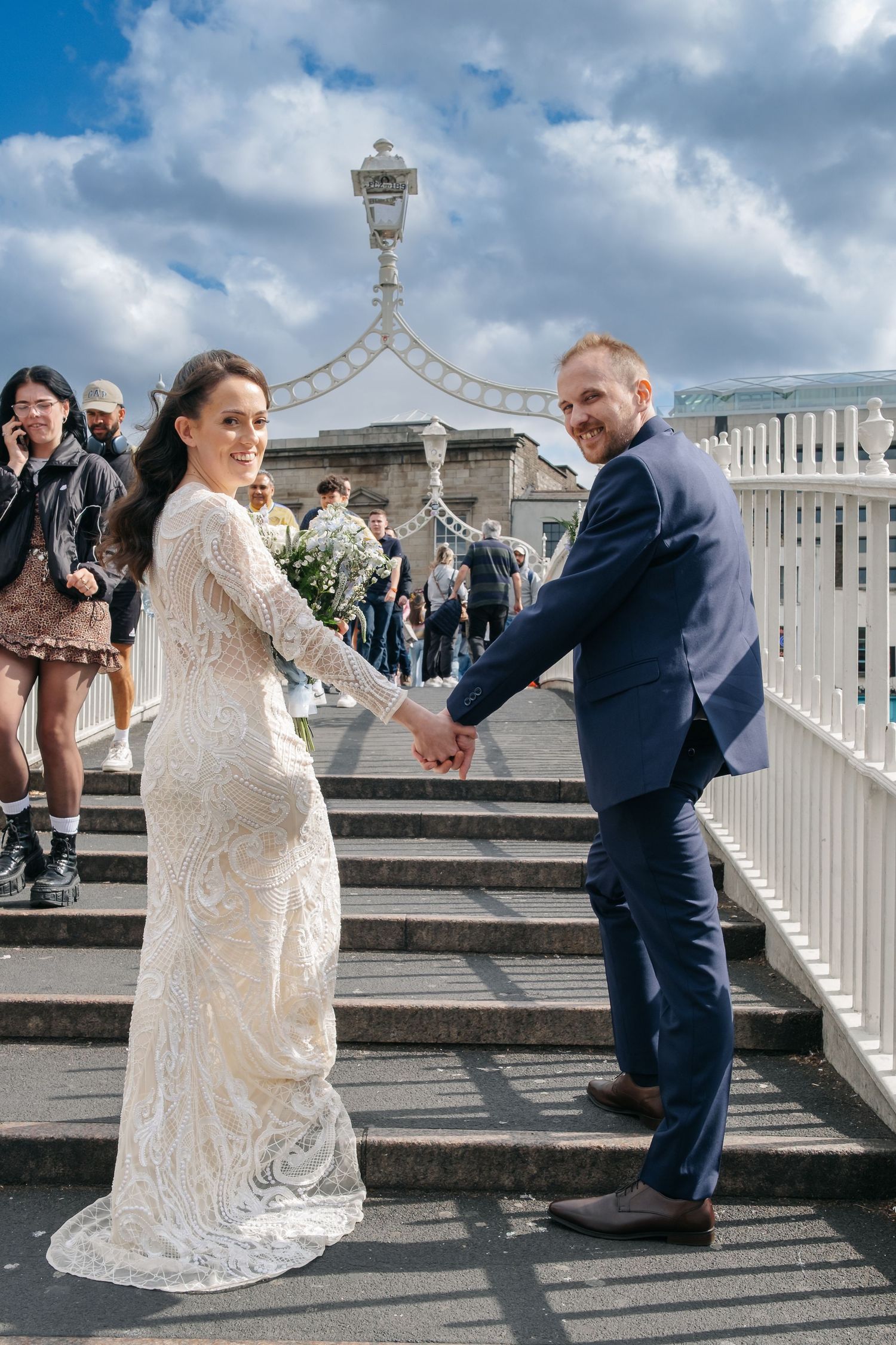 A couple posing on stone steps with ornate white railings under cloudy skies.