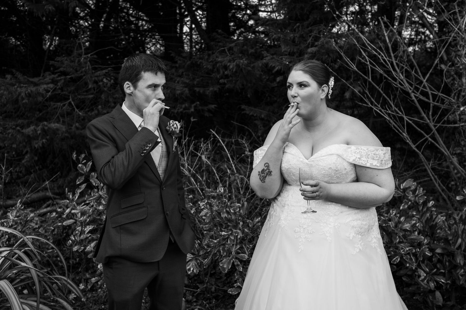 A candid black and white wedding moment between a couple sharing a laugh in a garden setting.
