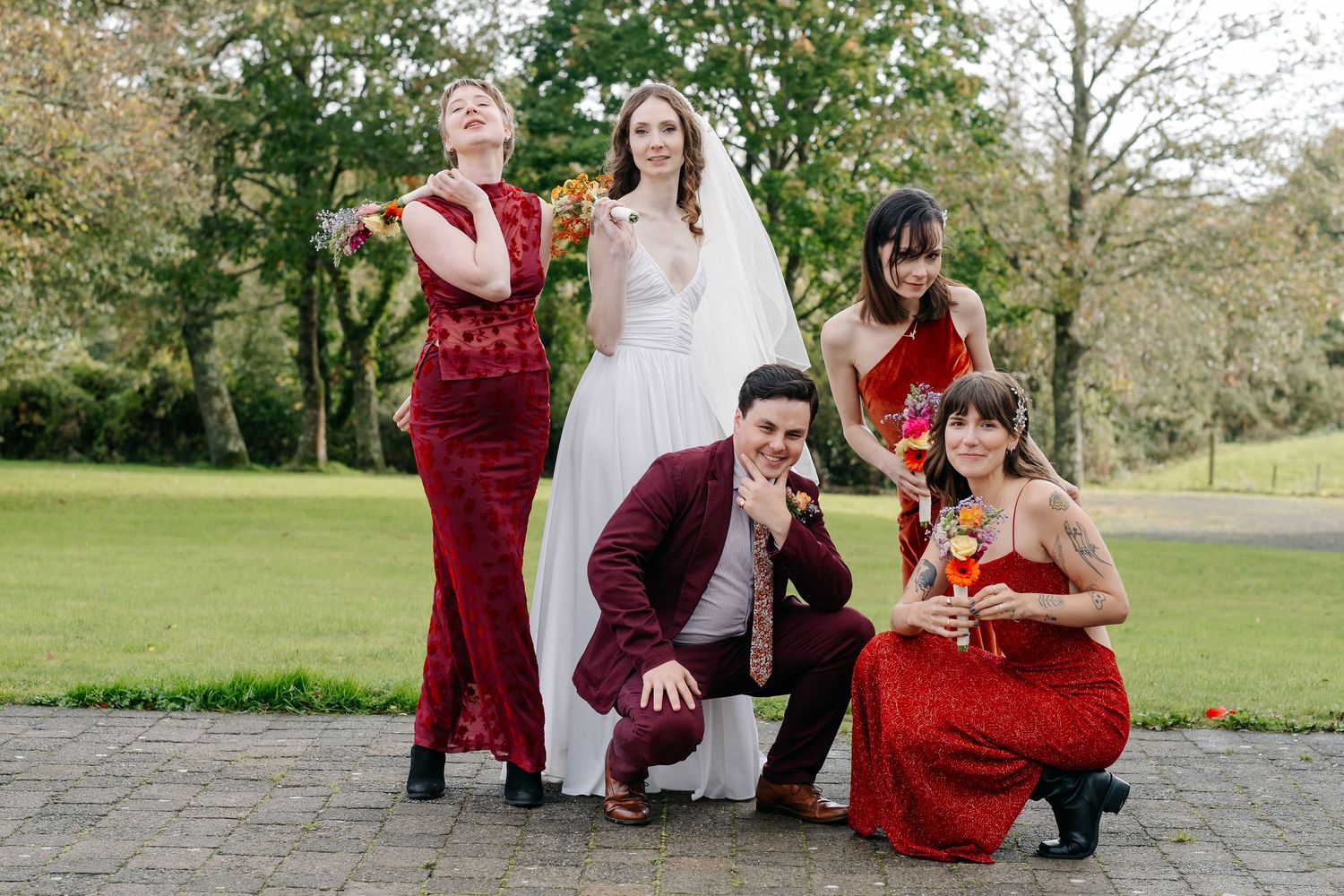 Wedding party in burgundy dresses and navy suits pose together outdoors on a sunny day.
